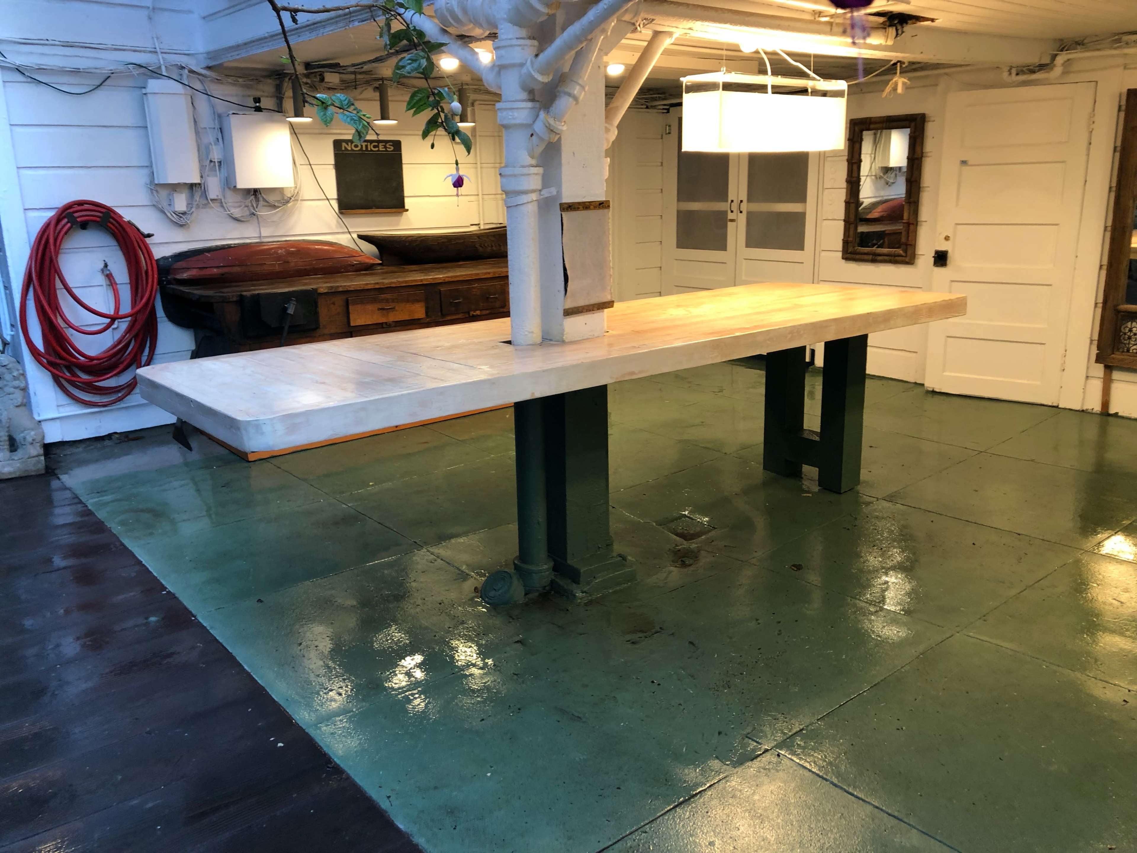 A spacious indoor area with a long table supported by green legs, accompanied by a wooden bench and a polished floor.