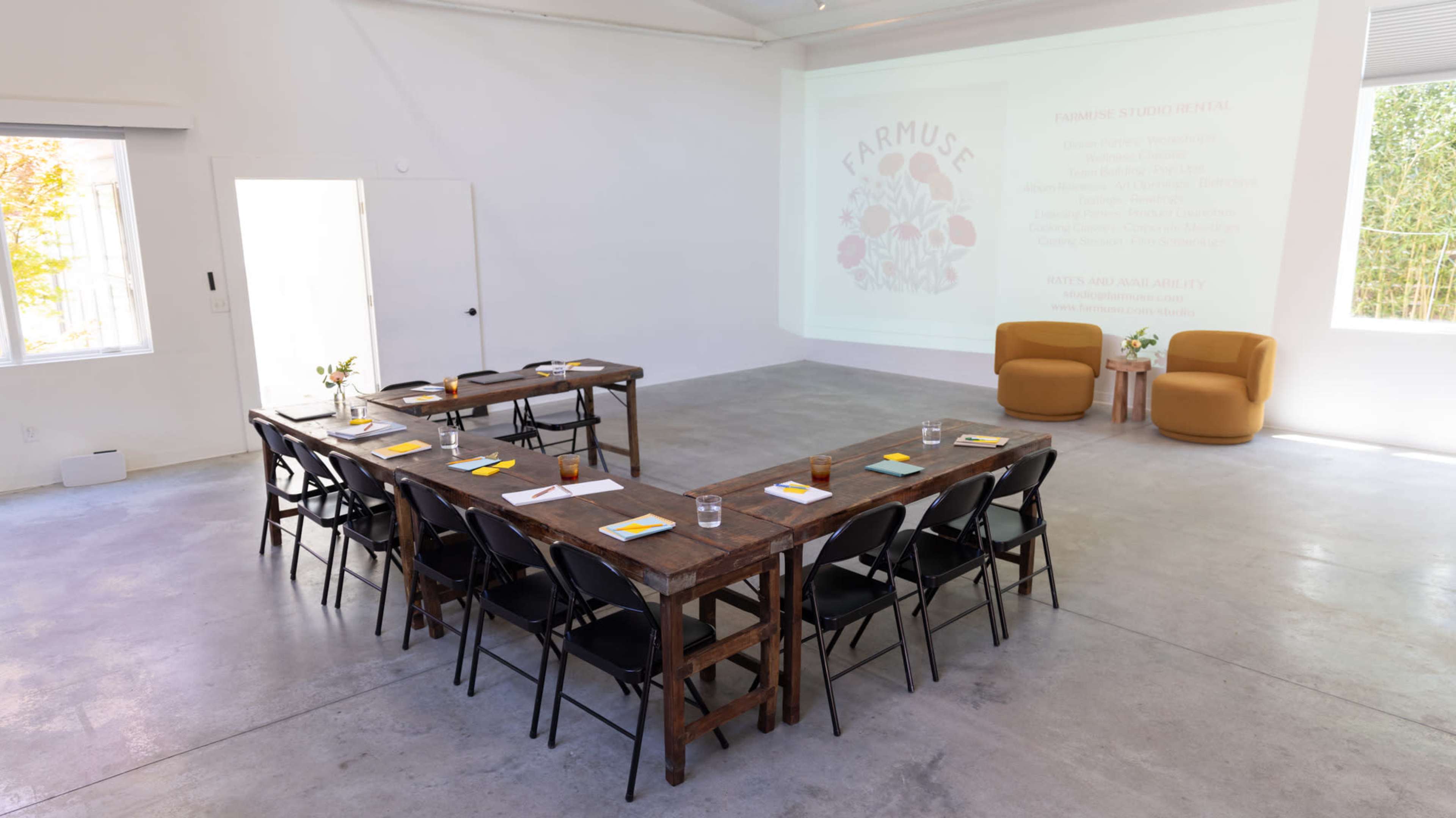 A meeting room is set up with a long wooden table, chairs, and a presentation screen displaying information about "FARMUSE" along with a pair of orange chairs in the background.