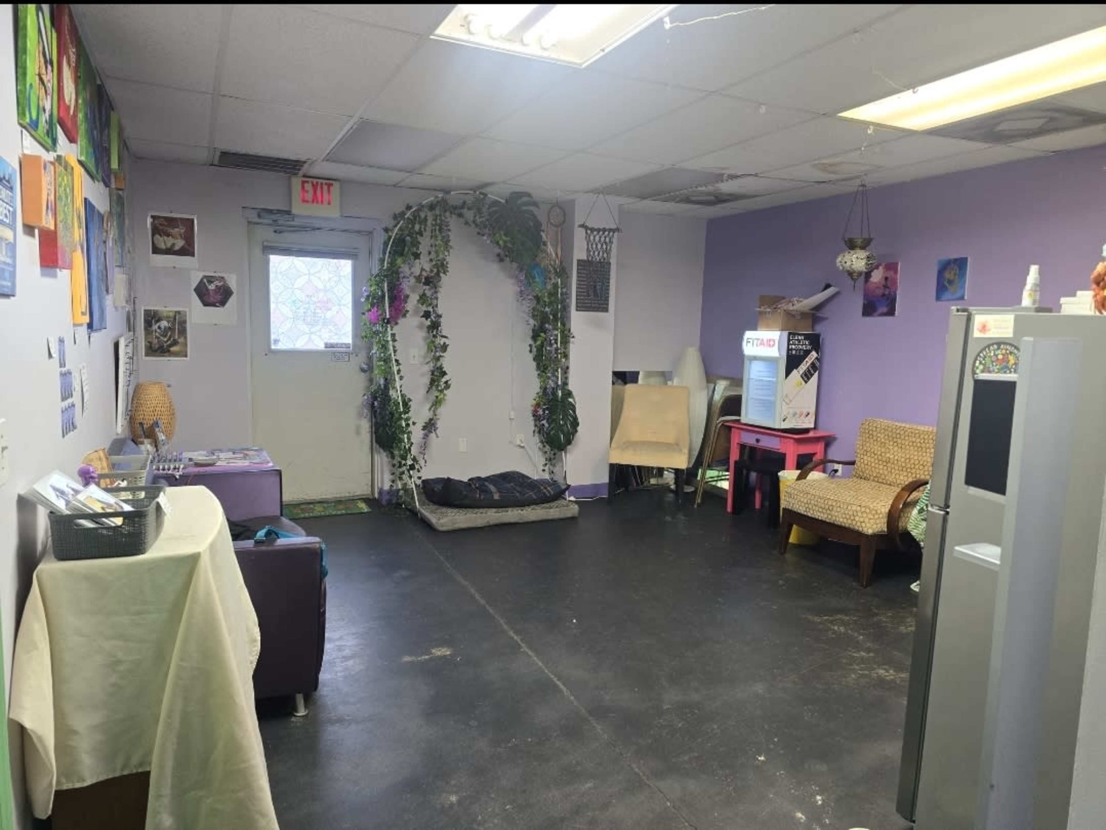 A room with purple walls, a door decorated with greenery, various furniture, and artwork displayed on the walls.
