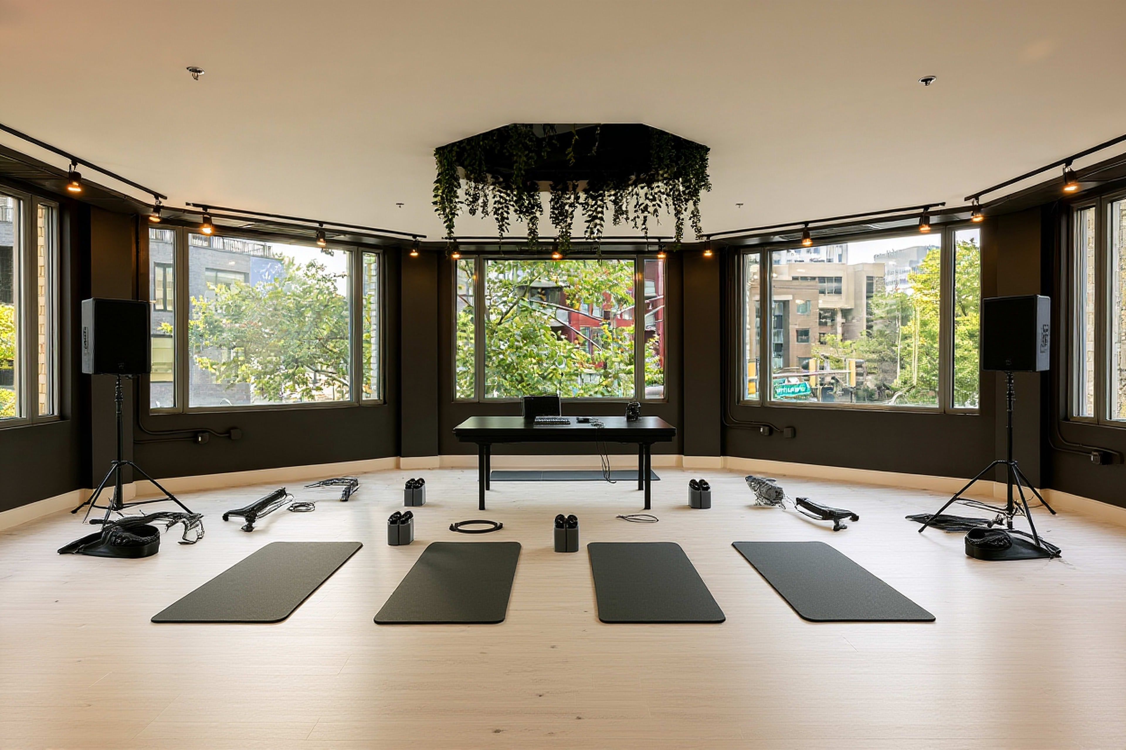 The image shows a spacious fitness studio equipped with exercise mats, weights, and various fitness equipment arranged symmetrically around the room.