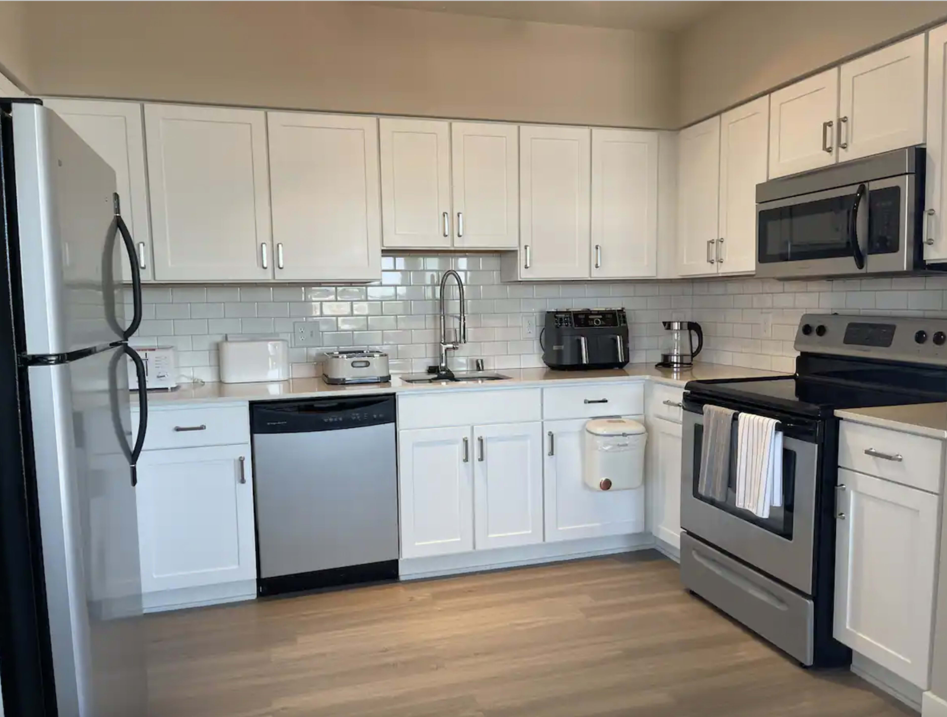 A modern kitchen features white cabinetry, stainless steel appliances, and a light-colored countertop.