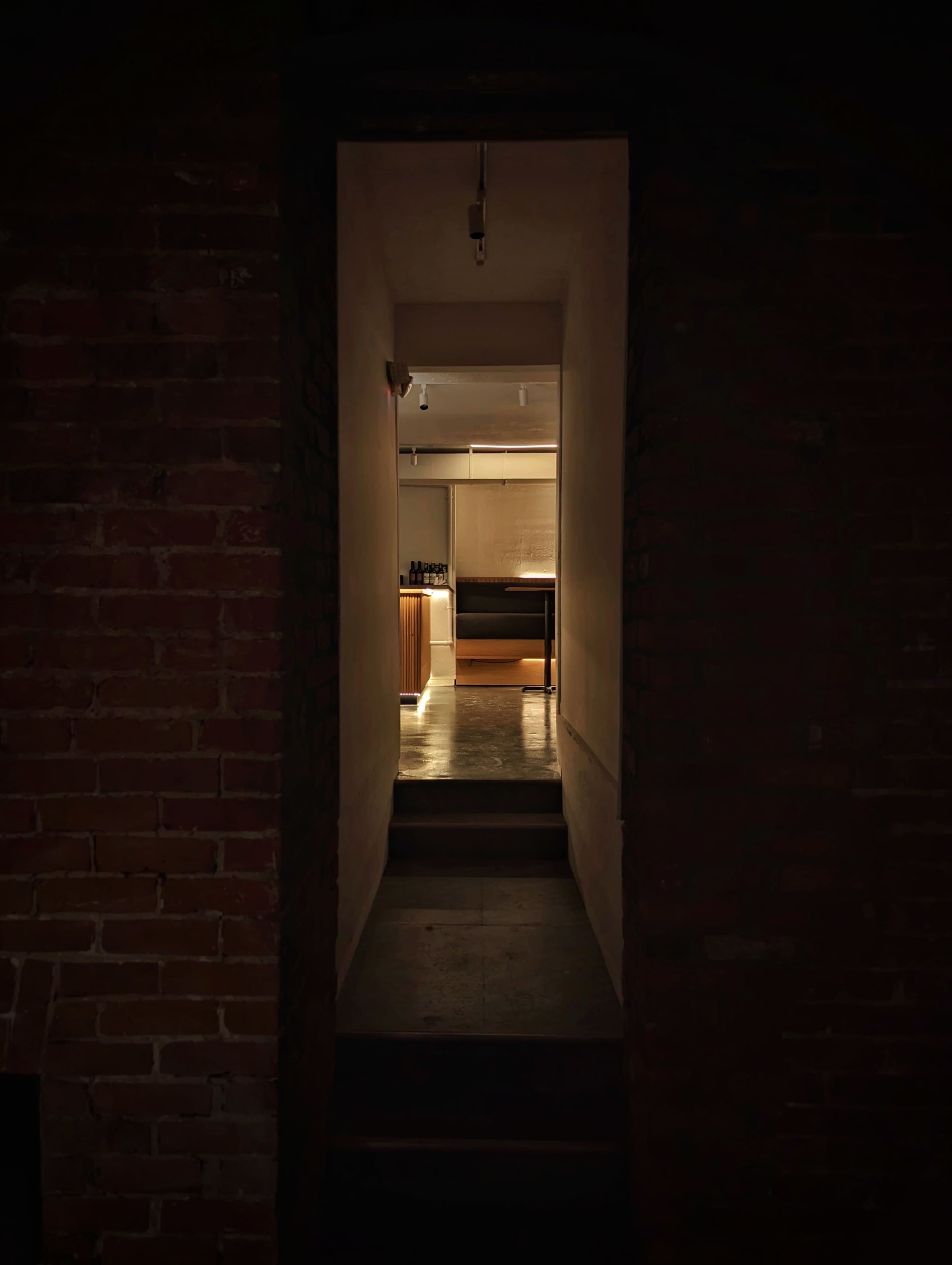 A dimly lit hallway leads to a modern kitchen illuminated by warm light.
