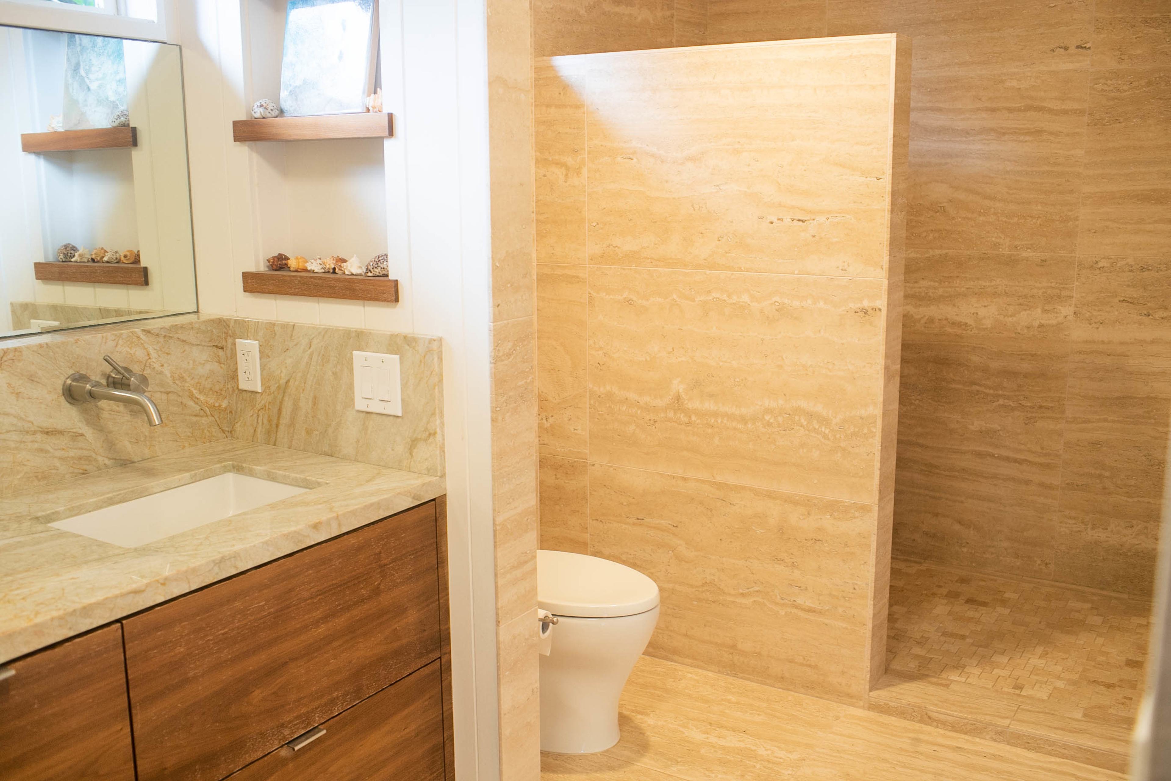 A modern bathroom featuring a stone shower, a wooden vanity with a sink, and a toilet.