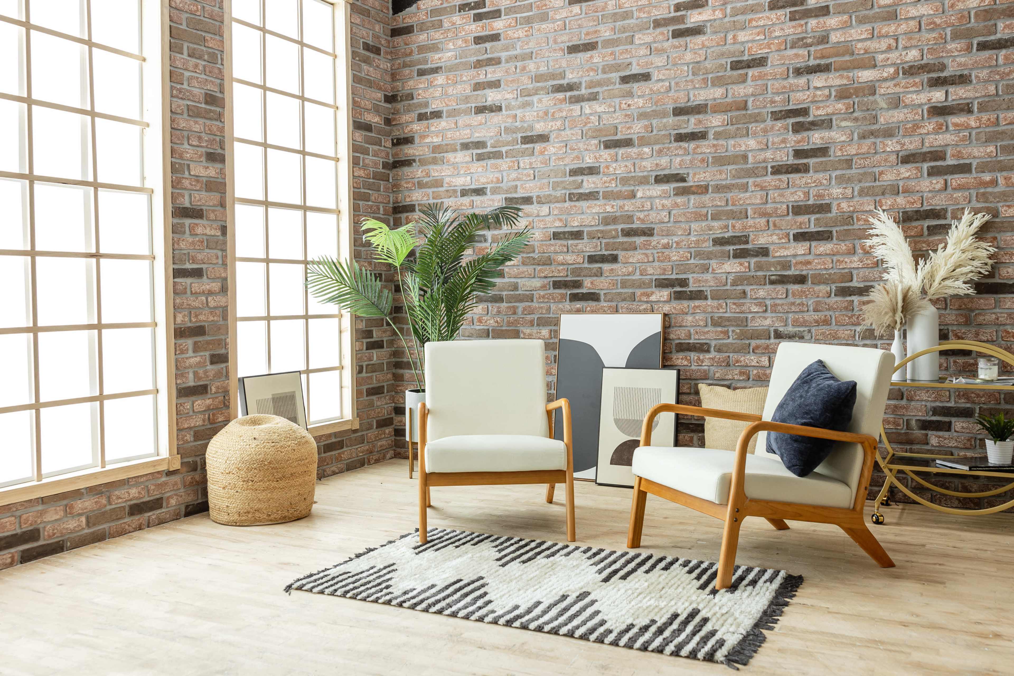 The scene features two modern chairs facing each other, with a large window and a brick wall in the background, alongside a plant and decorative items on the floor.