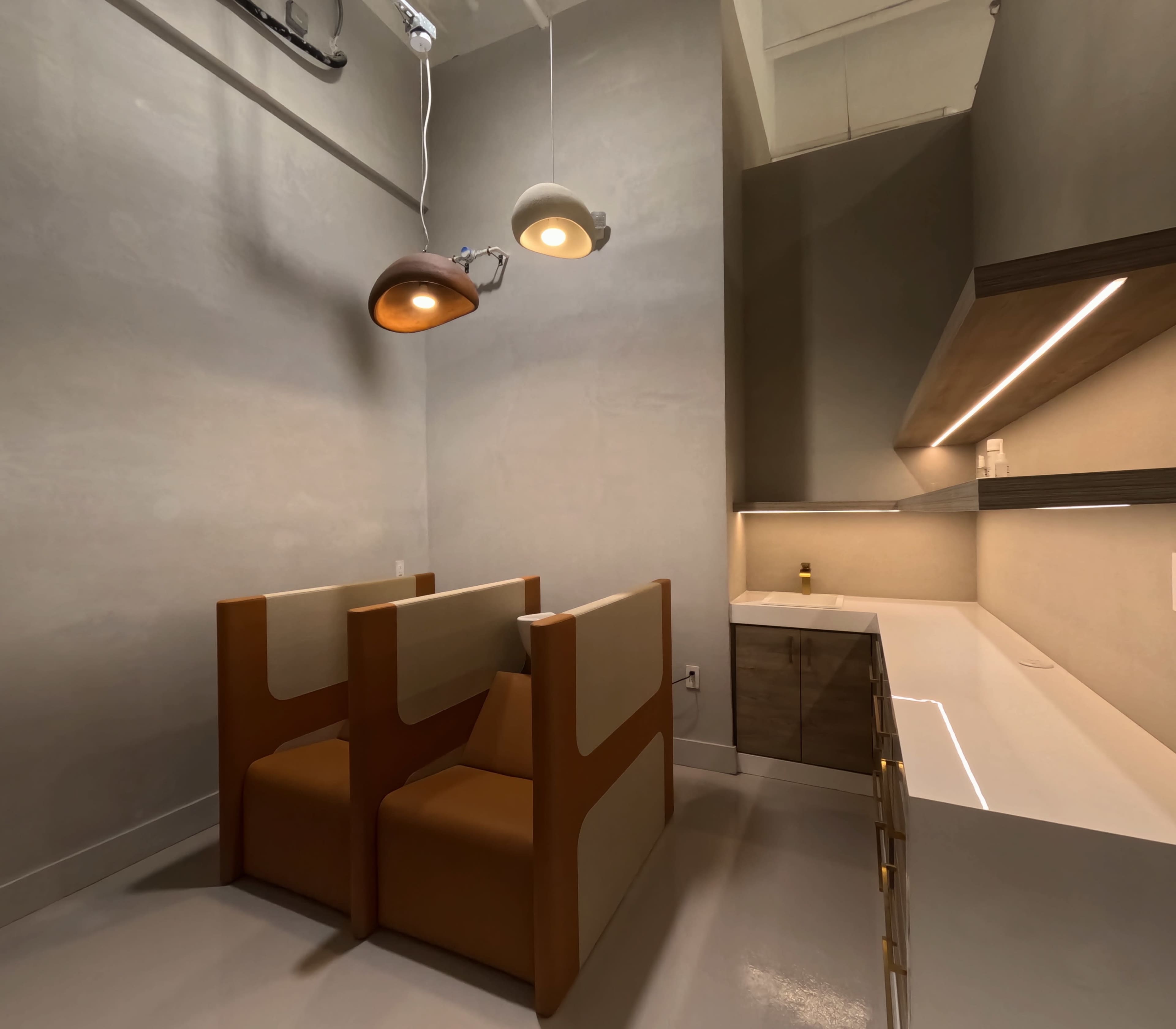 The image shows a modern, minimalist room featuring two enclosed seating booths and a sleek countertop area with lighting fixtures above.