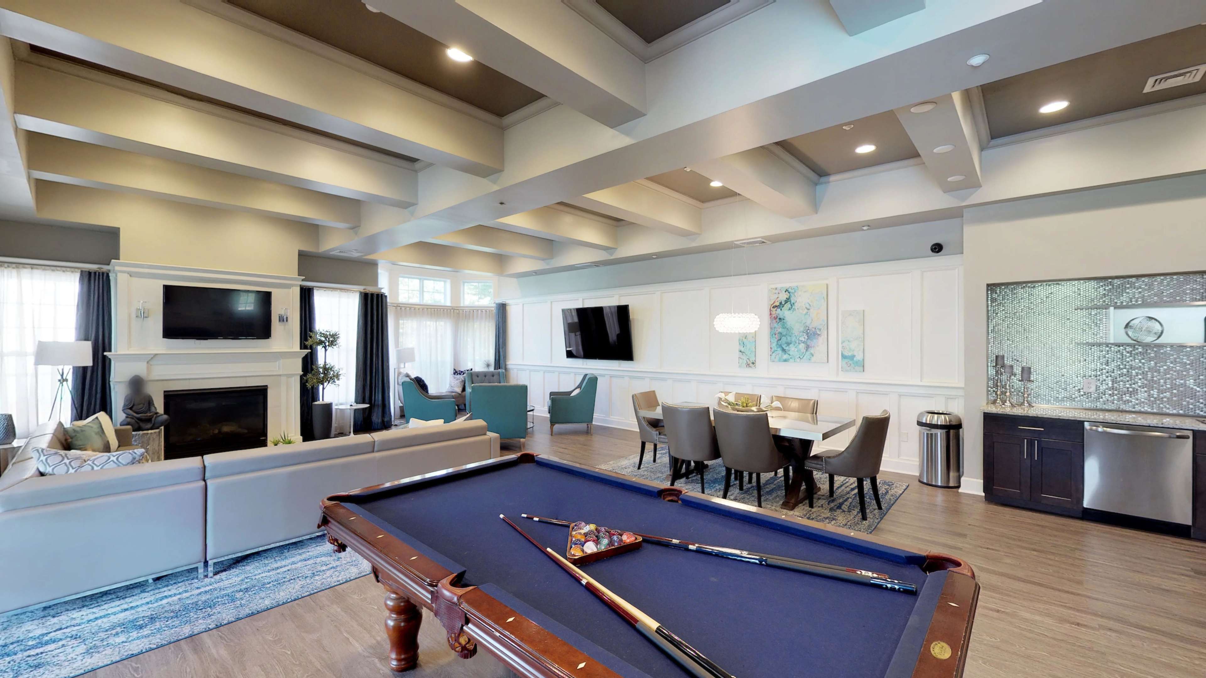 A spacious room features a billiard table in the foreground, a seating area with a fireplace, and a dining area with modern furnishings.