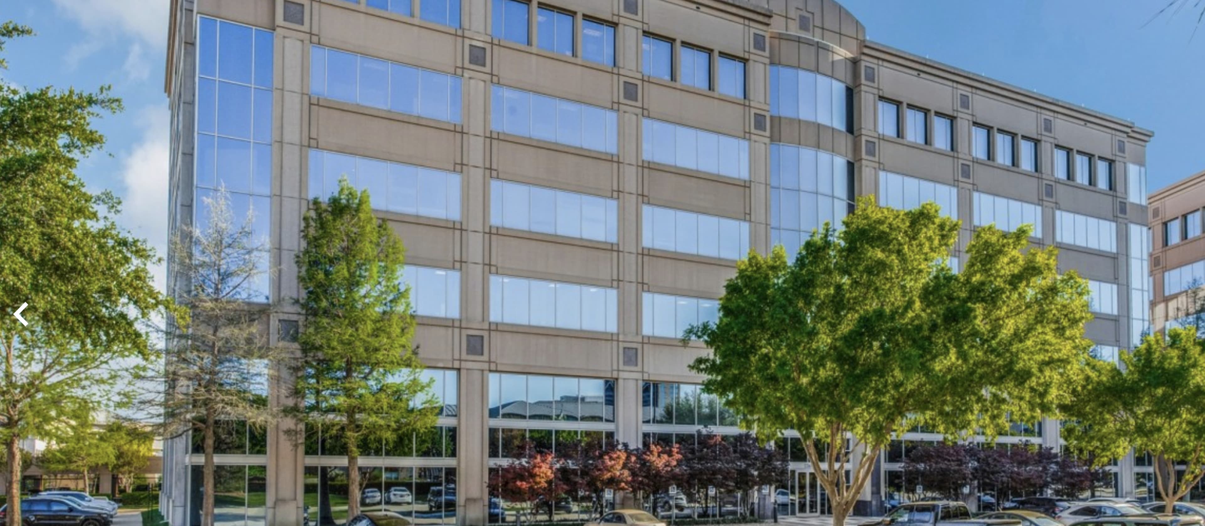 A modern office building with large glass windows and trees in front.