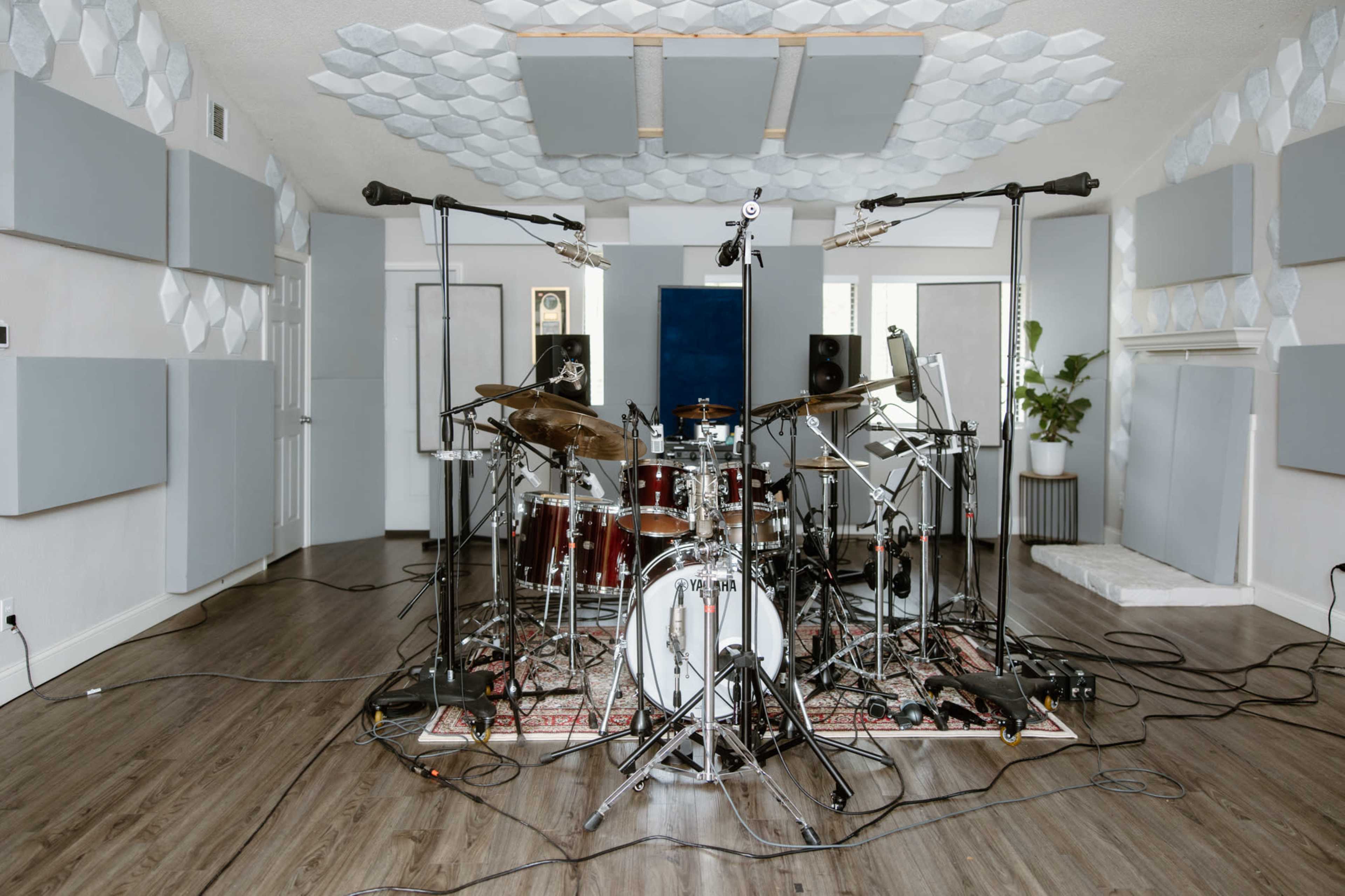 A recording studio with a drum set surrounded by soundproof panels and microphone stands on a wooden floor.