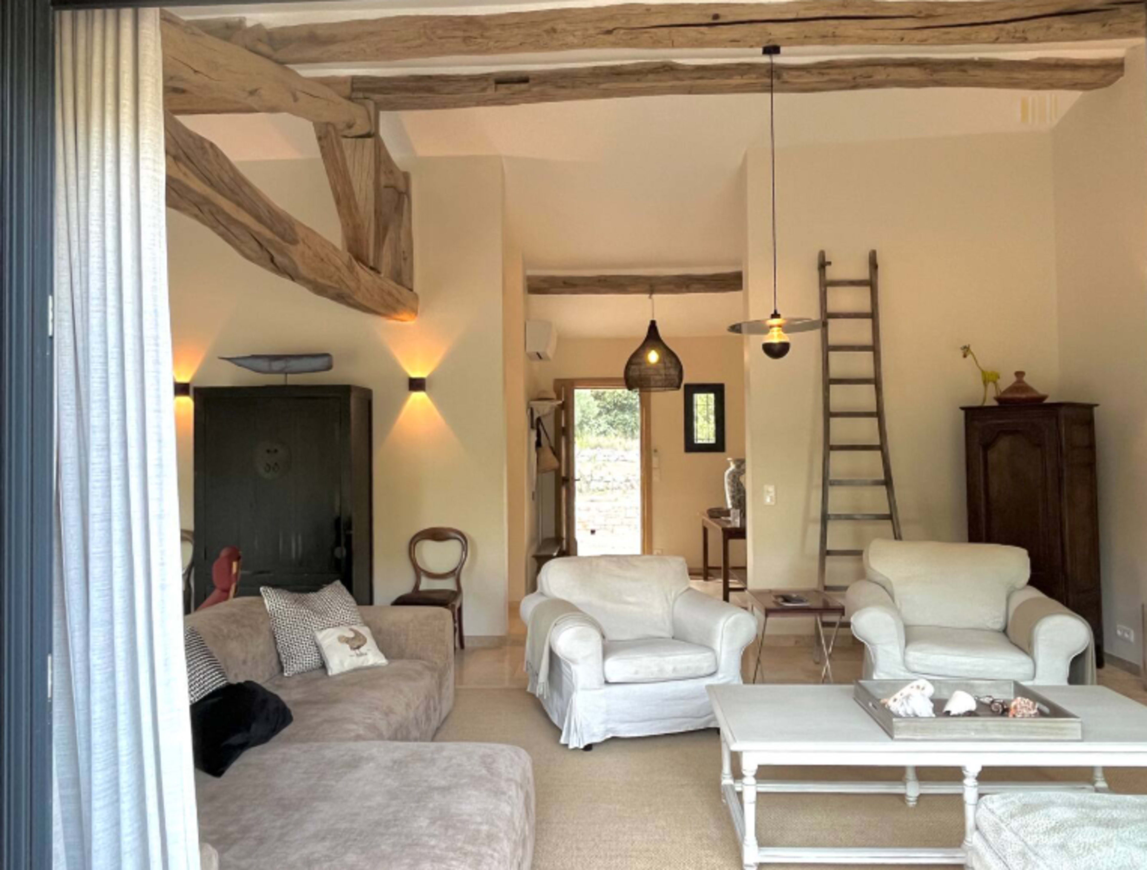 The image shows a cozy living room with wooden beams, comfortable furniture, and a ladder against the wall.