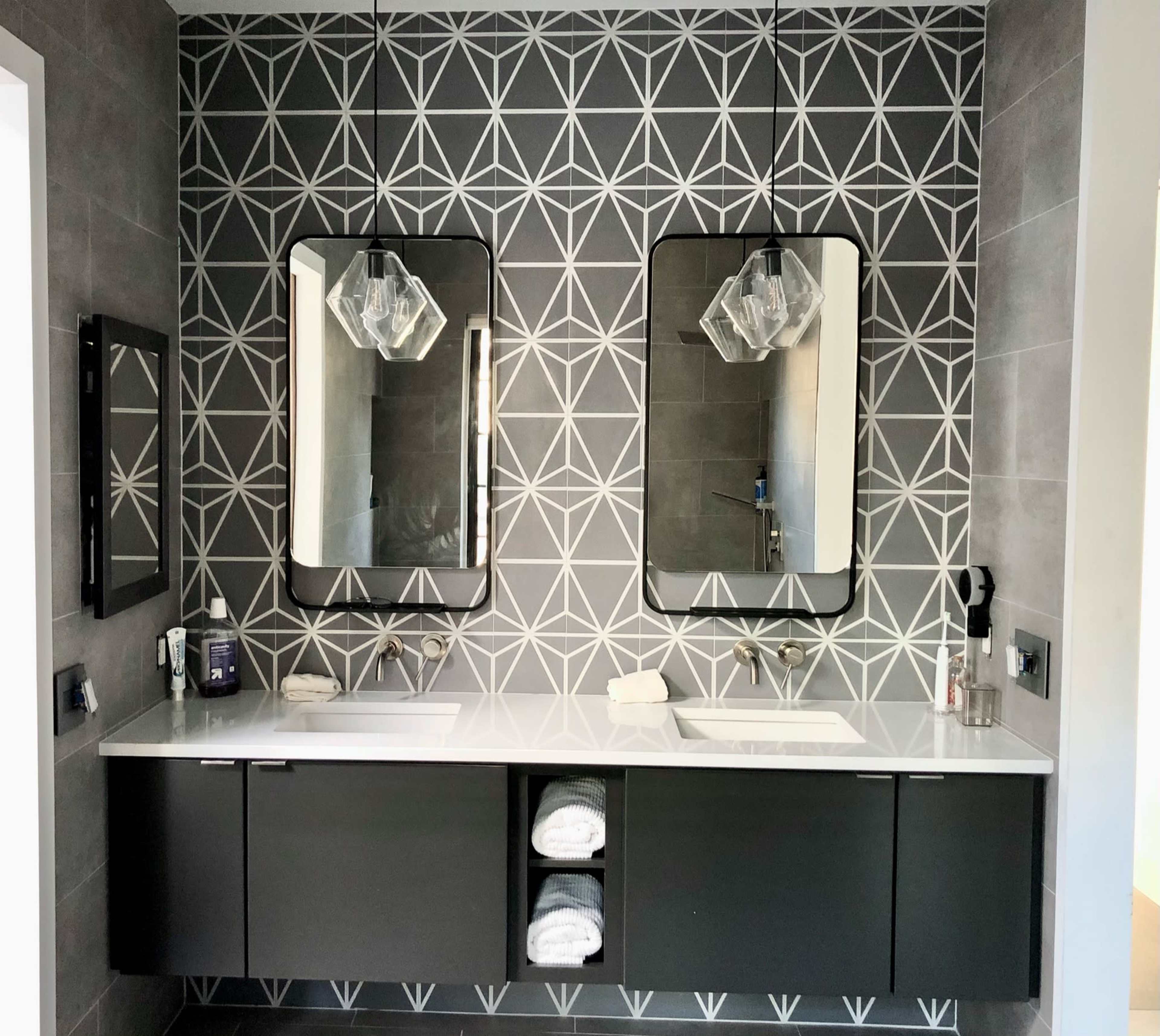 A modern bathroom with a double vanity, two mirrors, and geometric patterned tile on the wall.