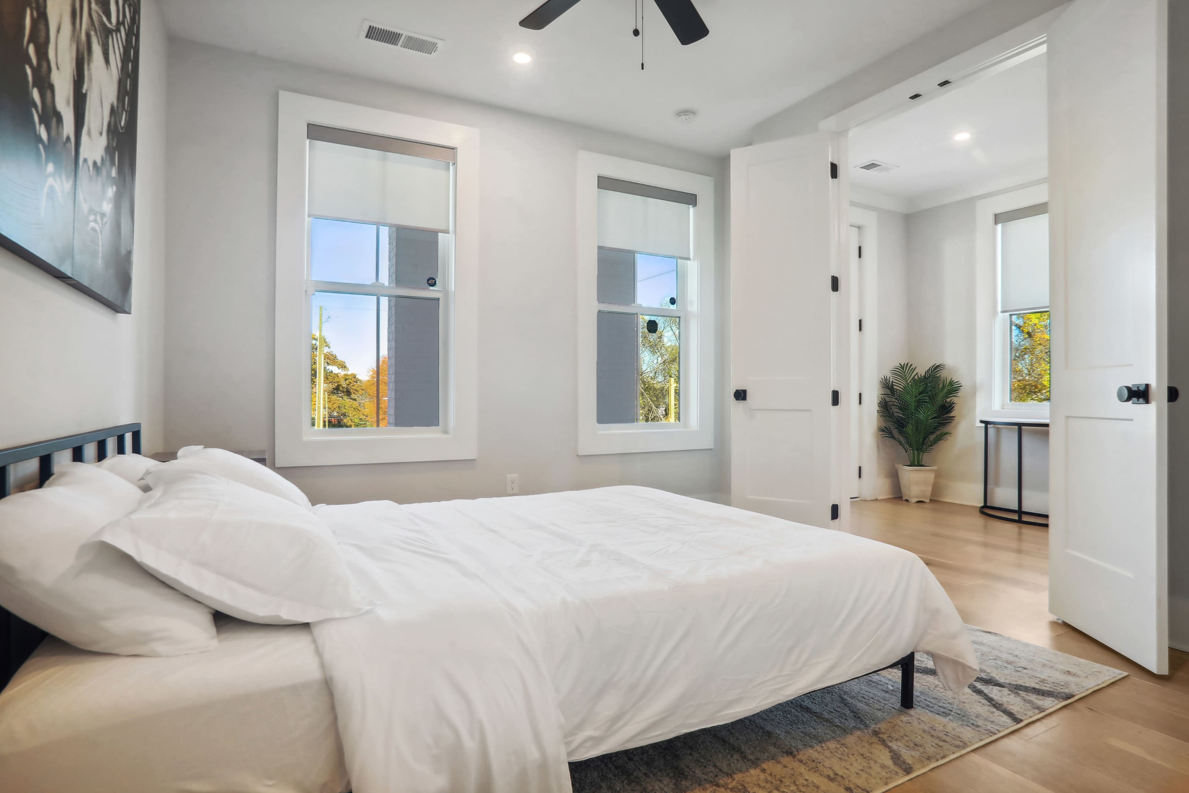 A bright bedroom with a bed, two windows, and a small desk in a corner.