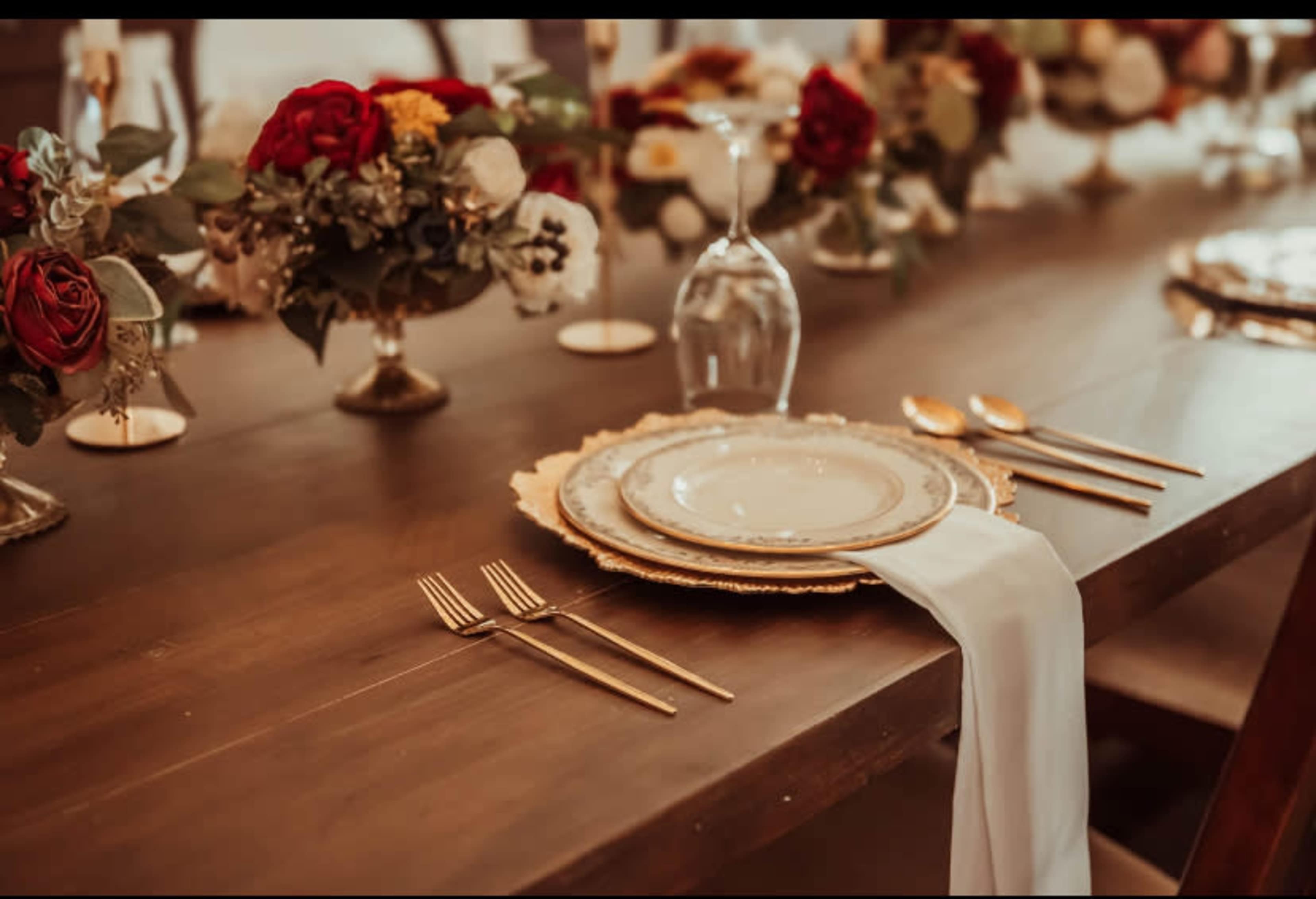 A long wooden table is elegantly set with gold-accented plates, silverware, and floral centerpieces.