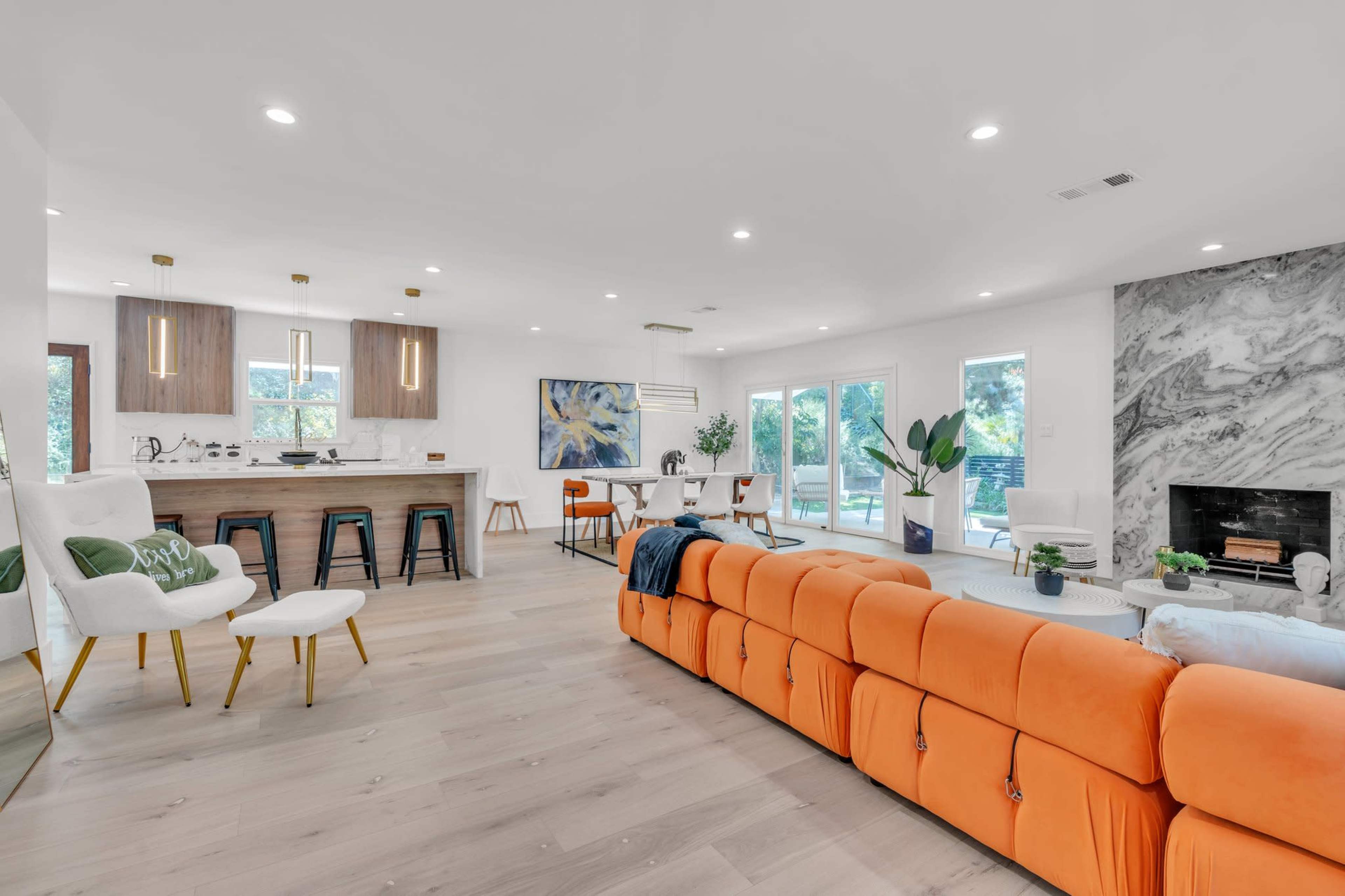 The open-concept living space features a modern kitchen with a large island, a dining area, and a bright seating area furnished with an orange sectional sofa.