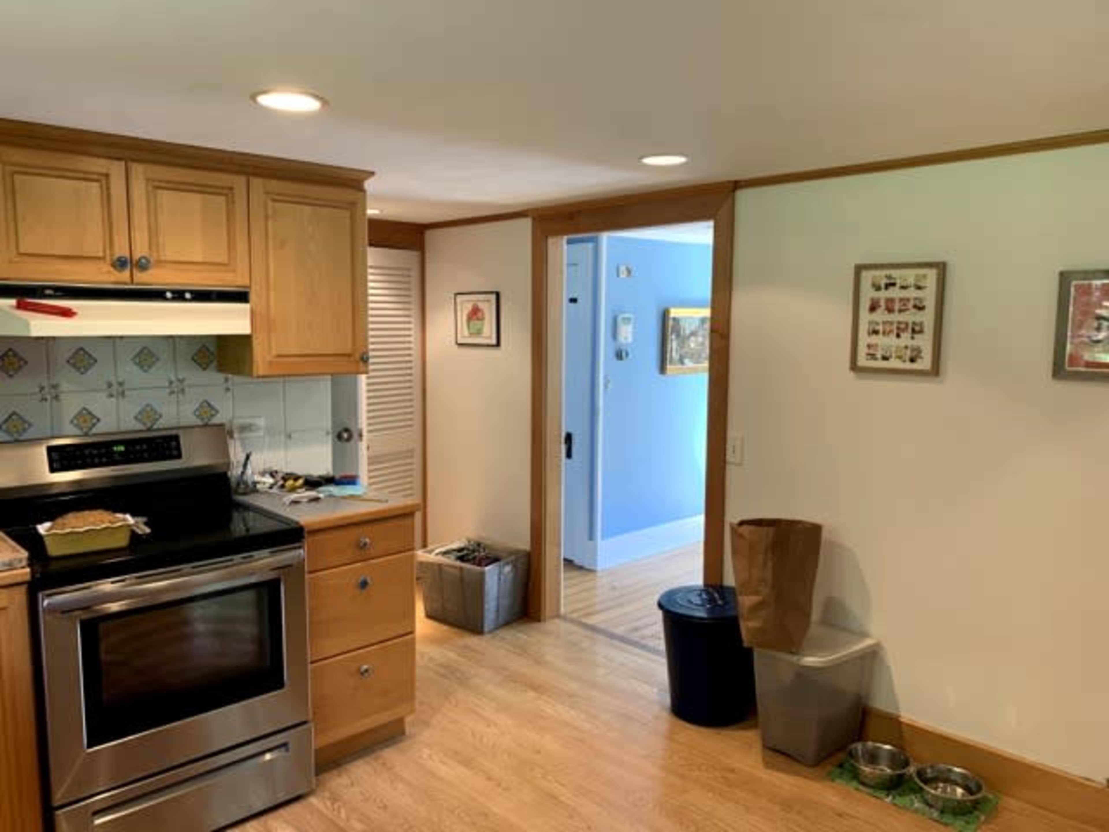 A kitchen features wooden cabinetry, a stainless steel stove, and a doorway leading to a blue wall room.
