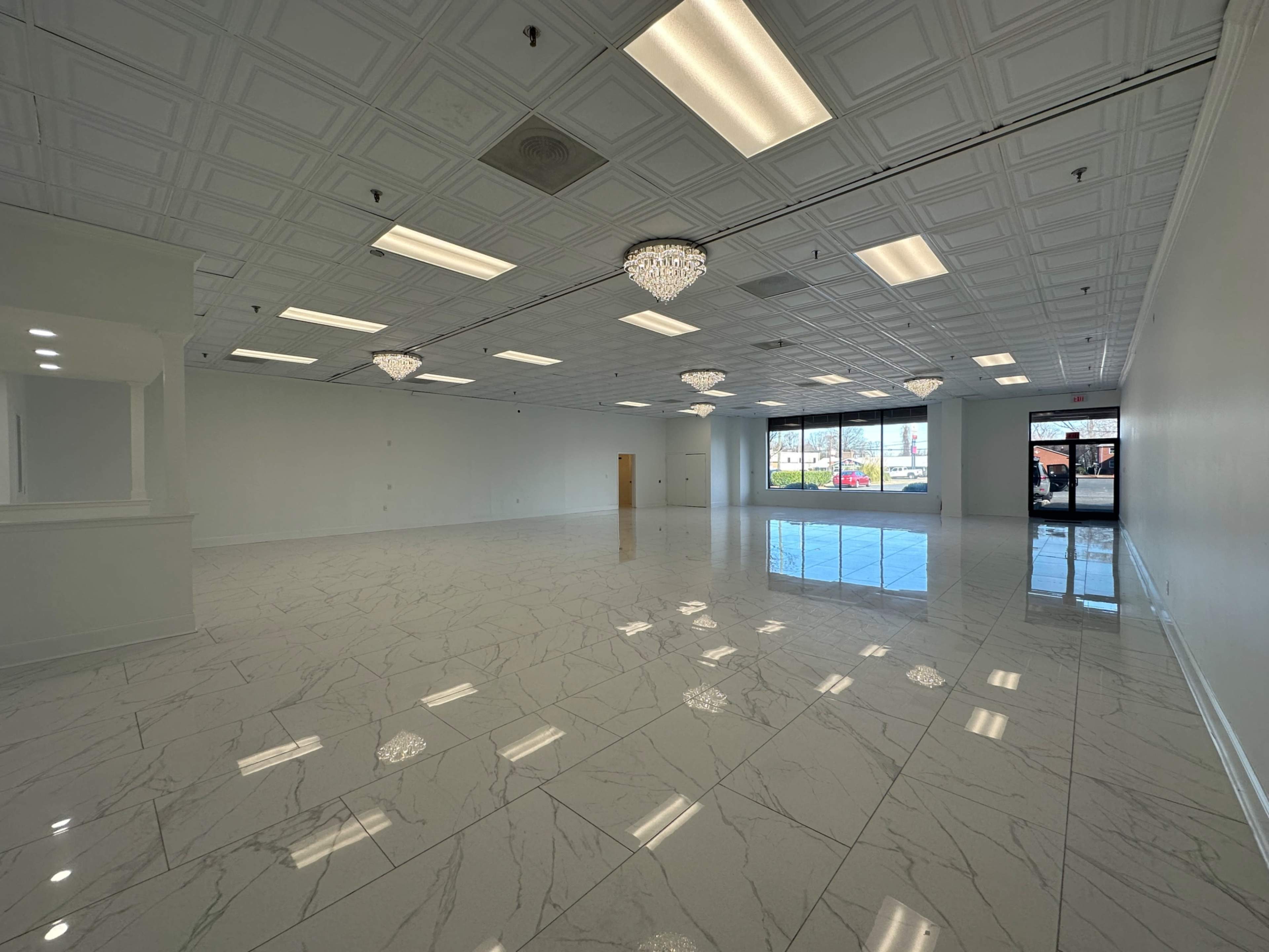 The image shows an empty commercial space with glossy tiled flooring, decorative ceiling tiles, and several crystal light fixtures.
