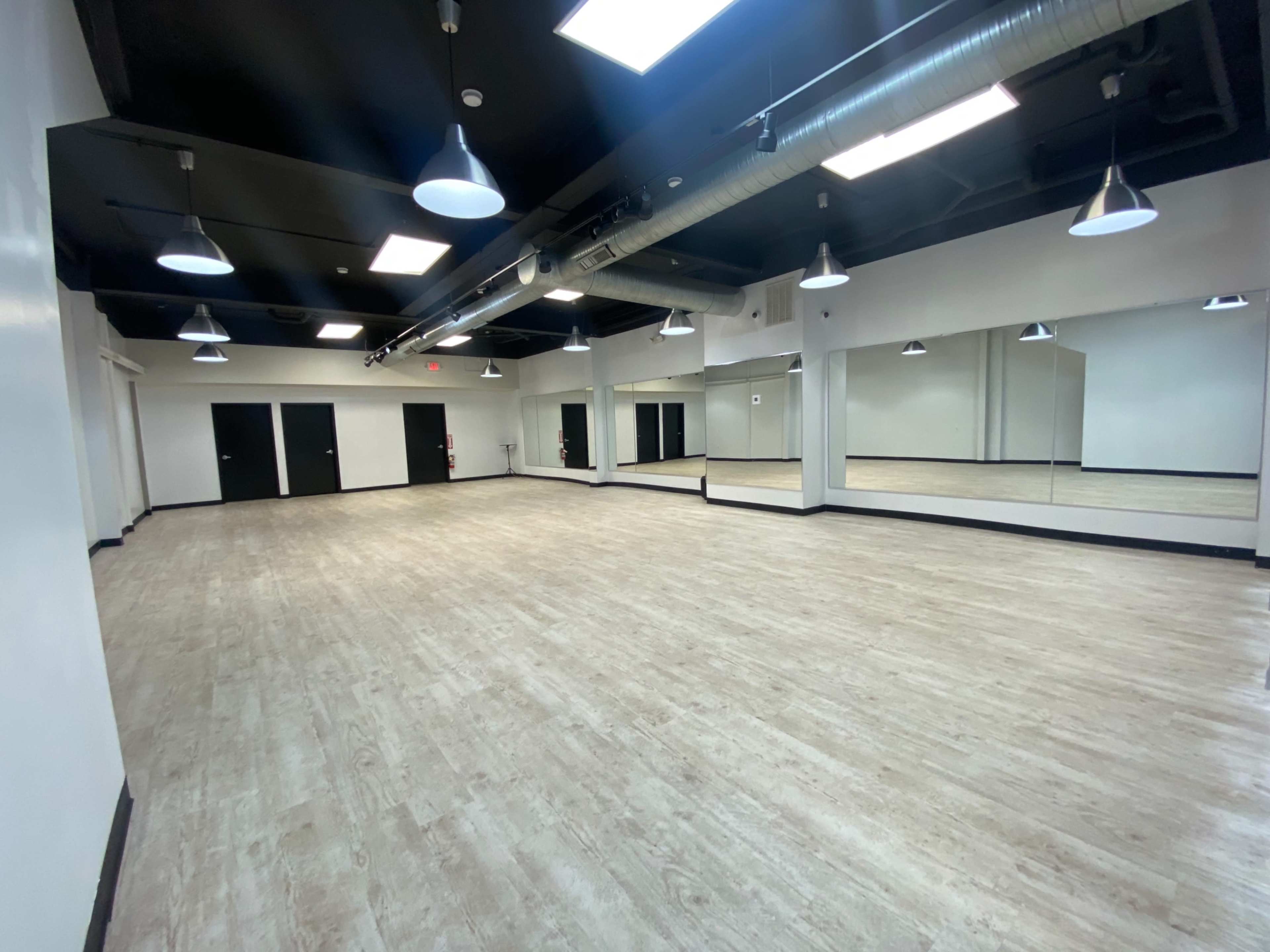 A spacious, well-lit studio with wooden flooring and large mirrors lining one wall.