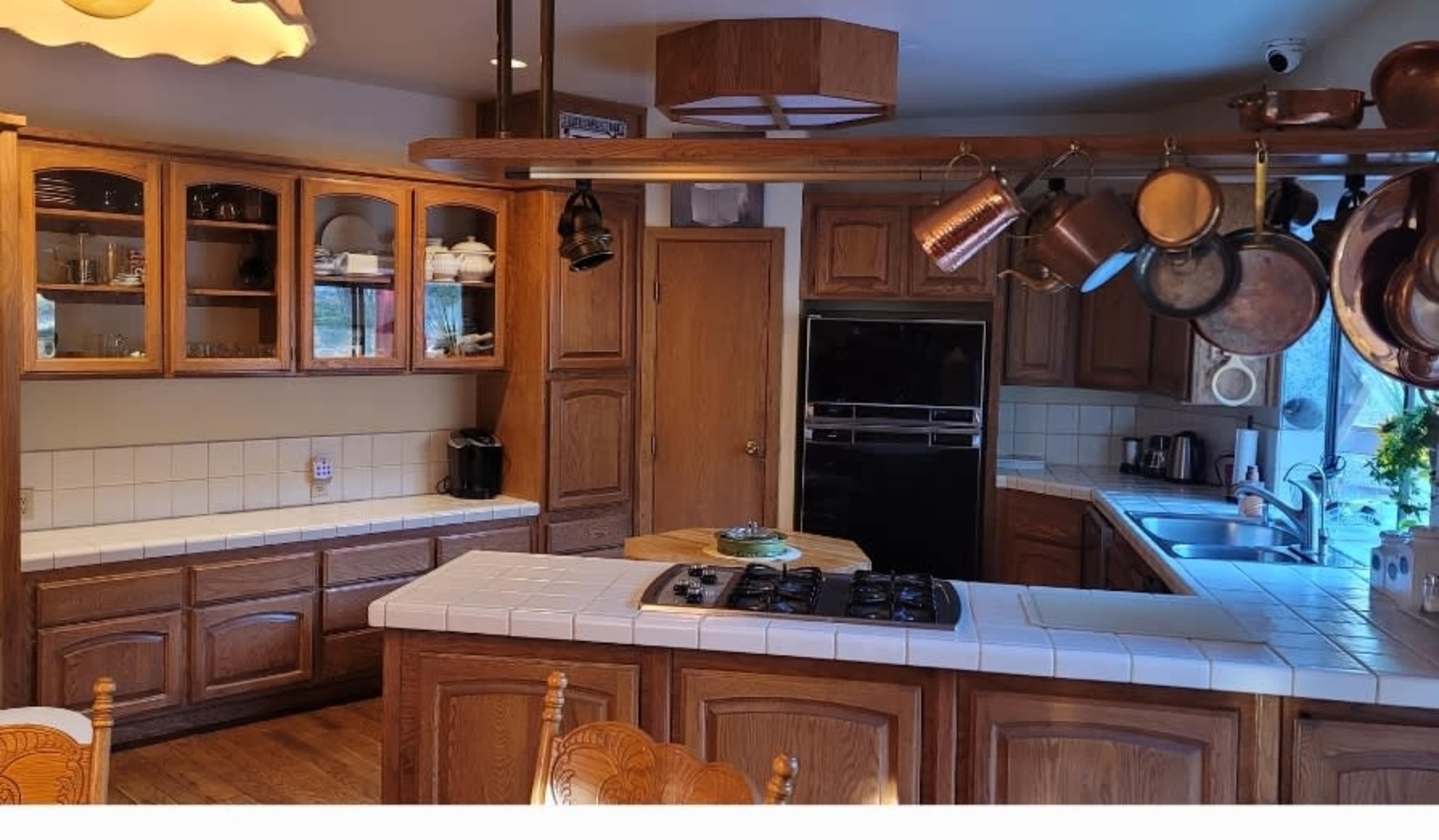 A wooden kitchen with a central island, equipped with a stove, and featuring cabinets filled with dishware.