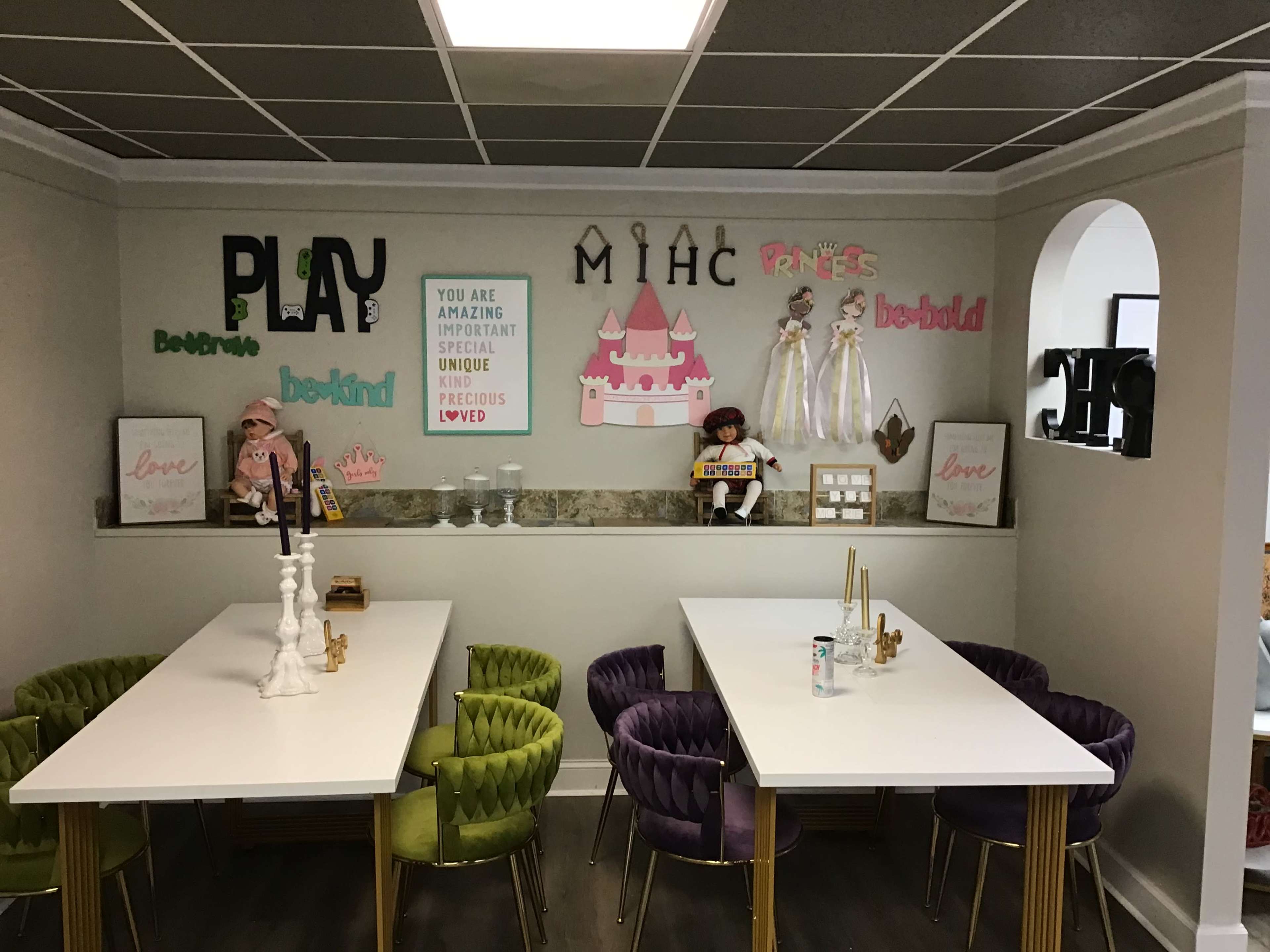 A brightly decorated room with two white tables, colorful chairs, and a wall adorned with playful signs and decorative items related to children's themes.