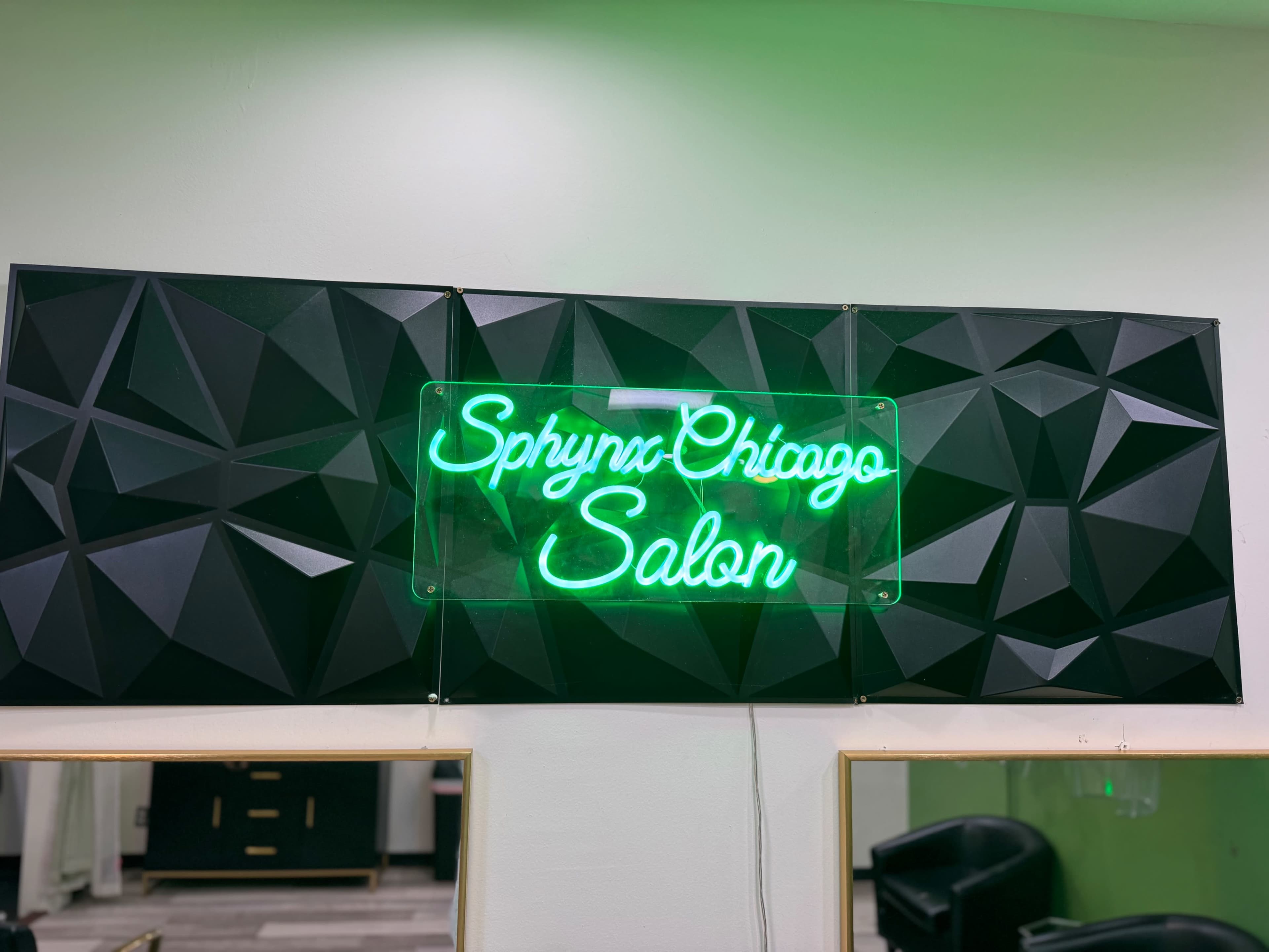The image features a neon green sign that reads "Sphynx Chicago Salon" mounted on a textured black background within a salon setting.