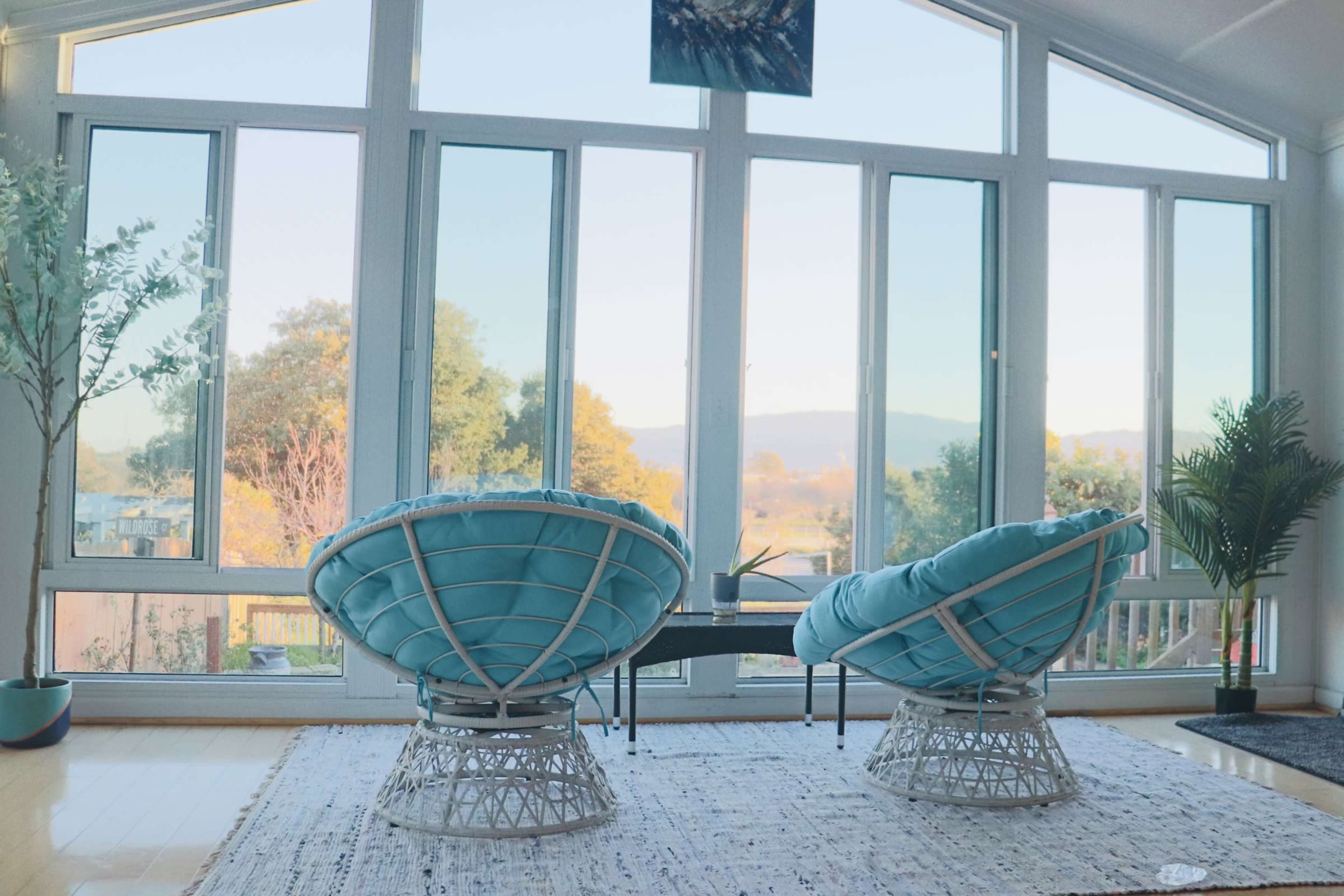 Two turquoise chairs are positioned facing large windows that overlook a scenic view of mountains and trees.