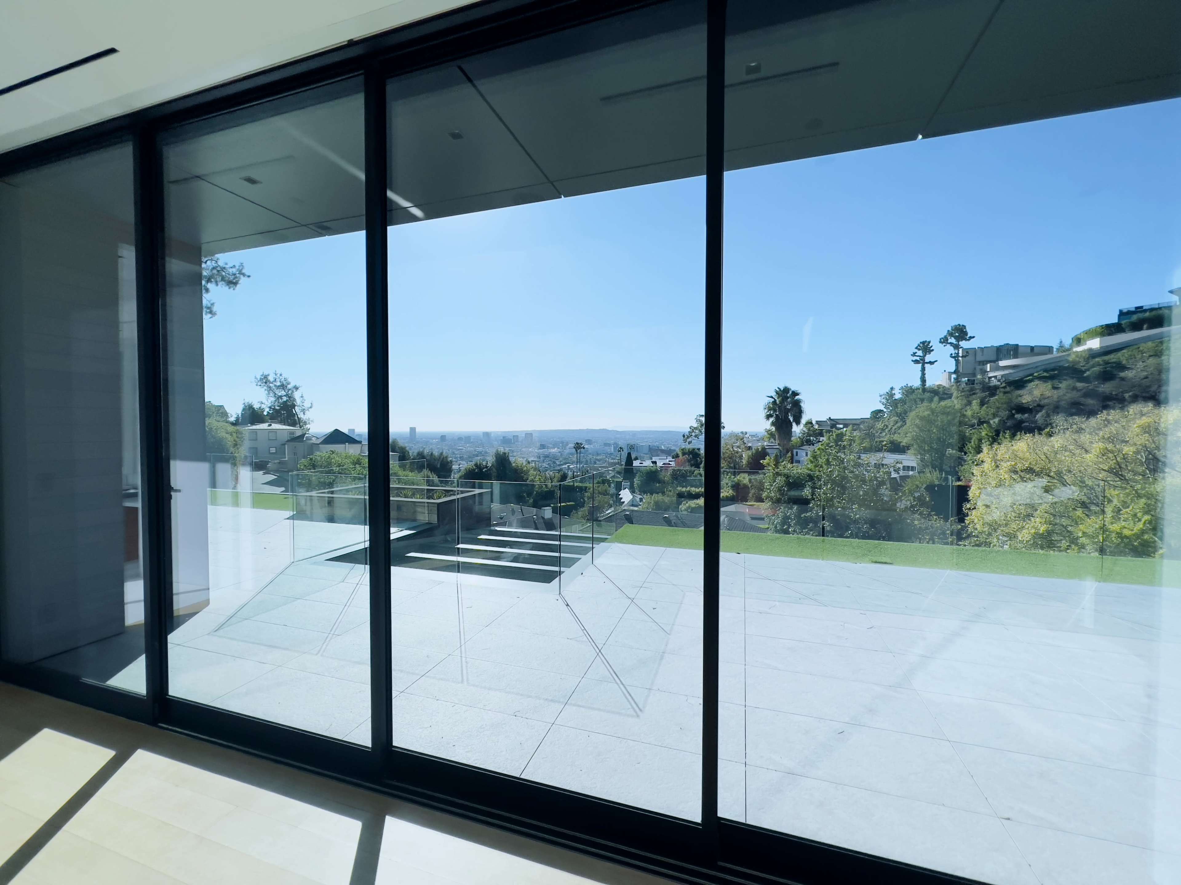 A large glass window providing a view of a landscaped yard and distant city skyline under clear blue skies.