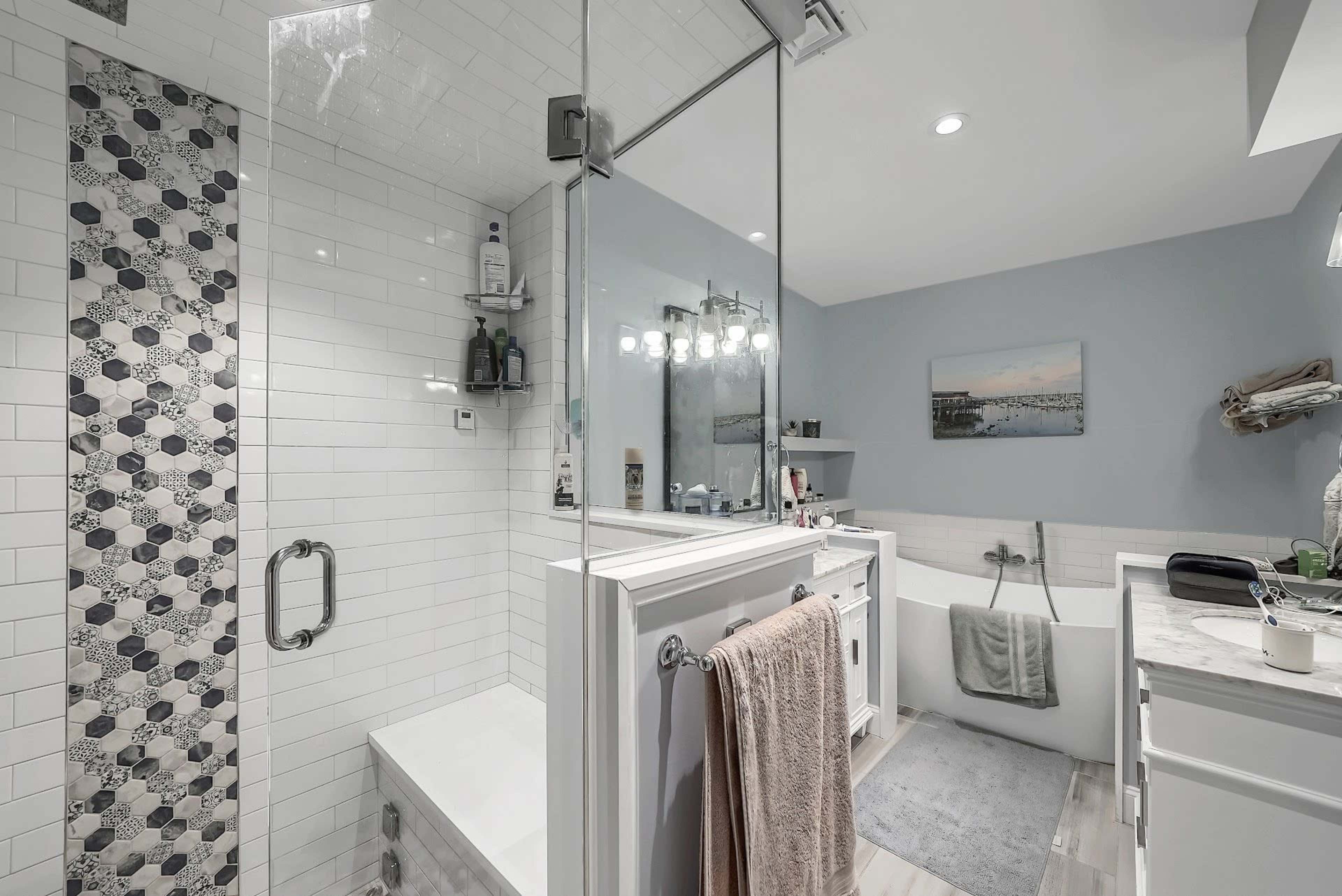 A modern bathroom features a glass shower, a freestanding bathtub, and a dual sink vanity with a decorative mirror.