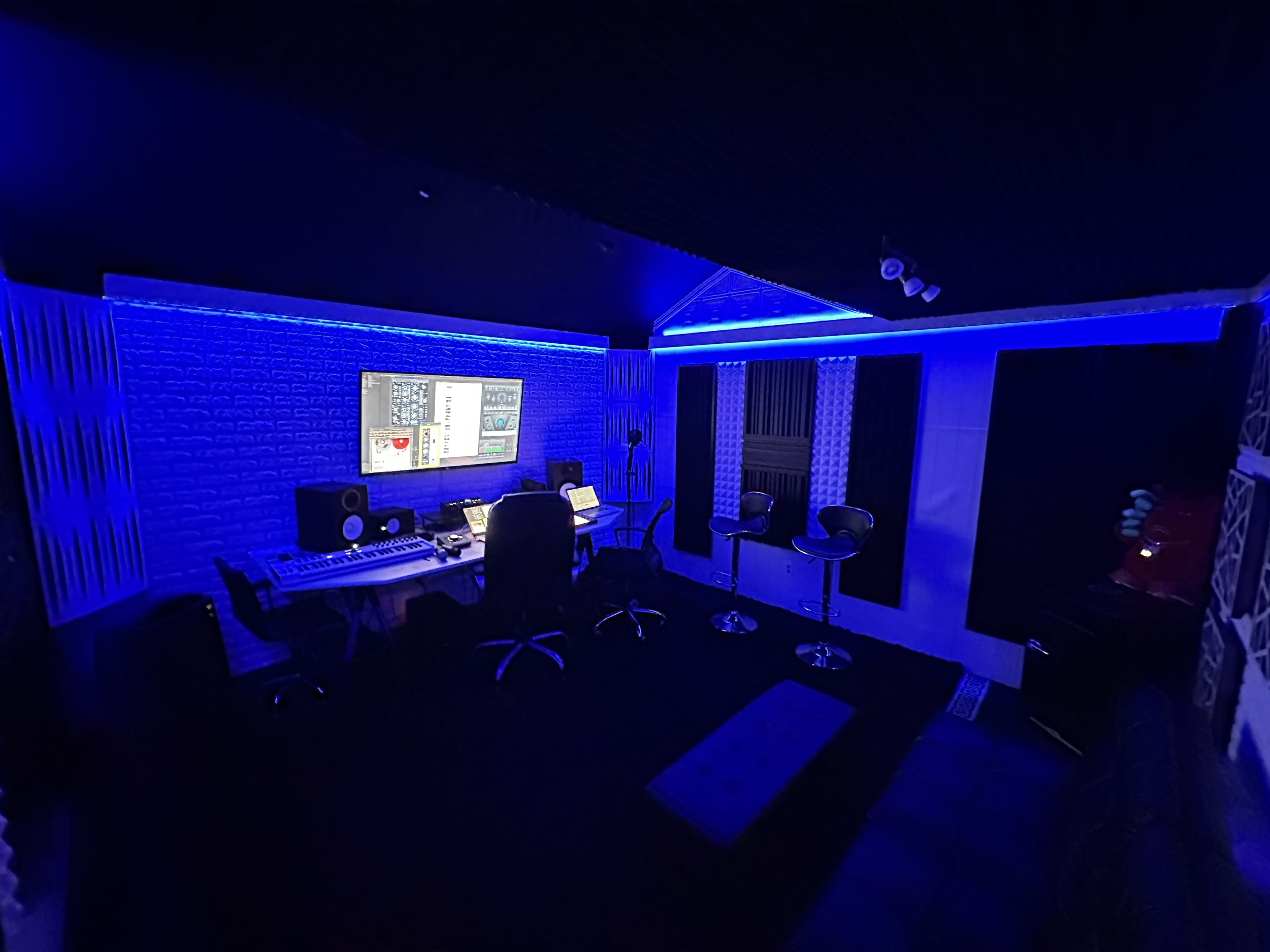The image shows a modern music studio with blue LED lighting, a computer setup, and audio equipment arranged around a central workspace.