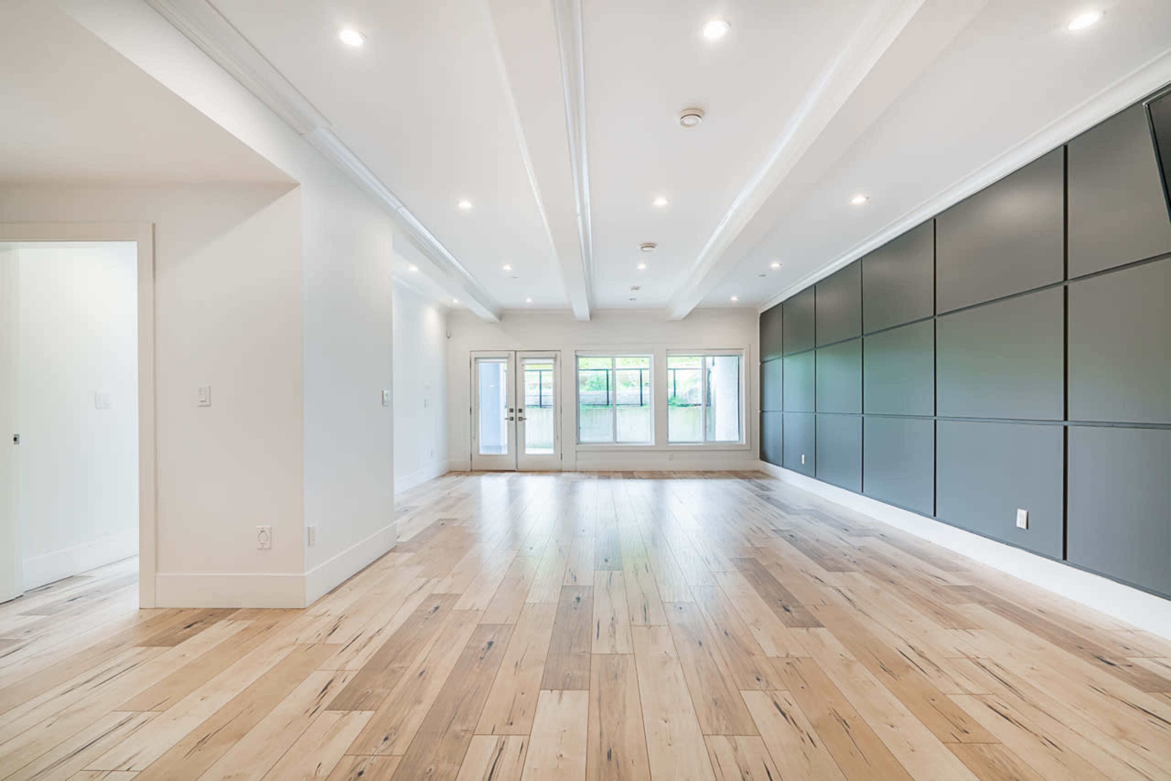 The spacious room features hardwood flooring, recessed lighting, and large windows along one wall.