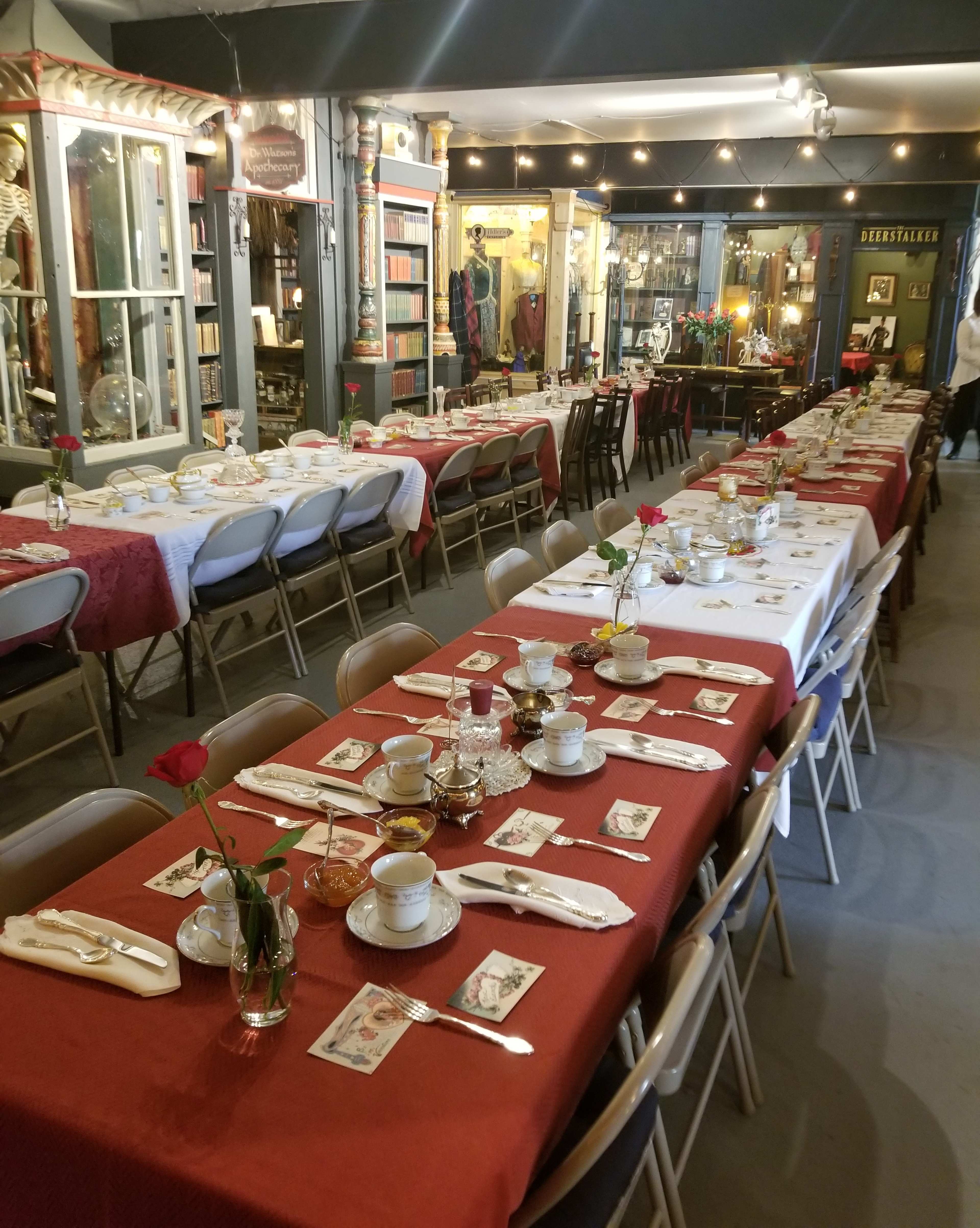 A long dining table is set with dishes, utensils, and flowers, surrounded by vintage decor and displays in a shop interior.