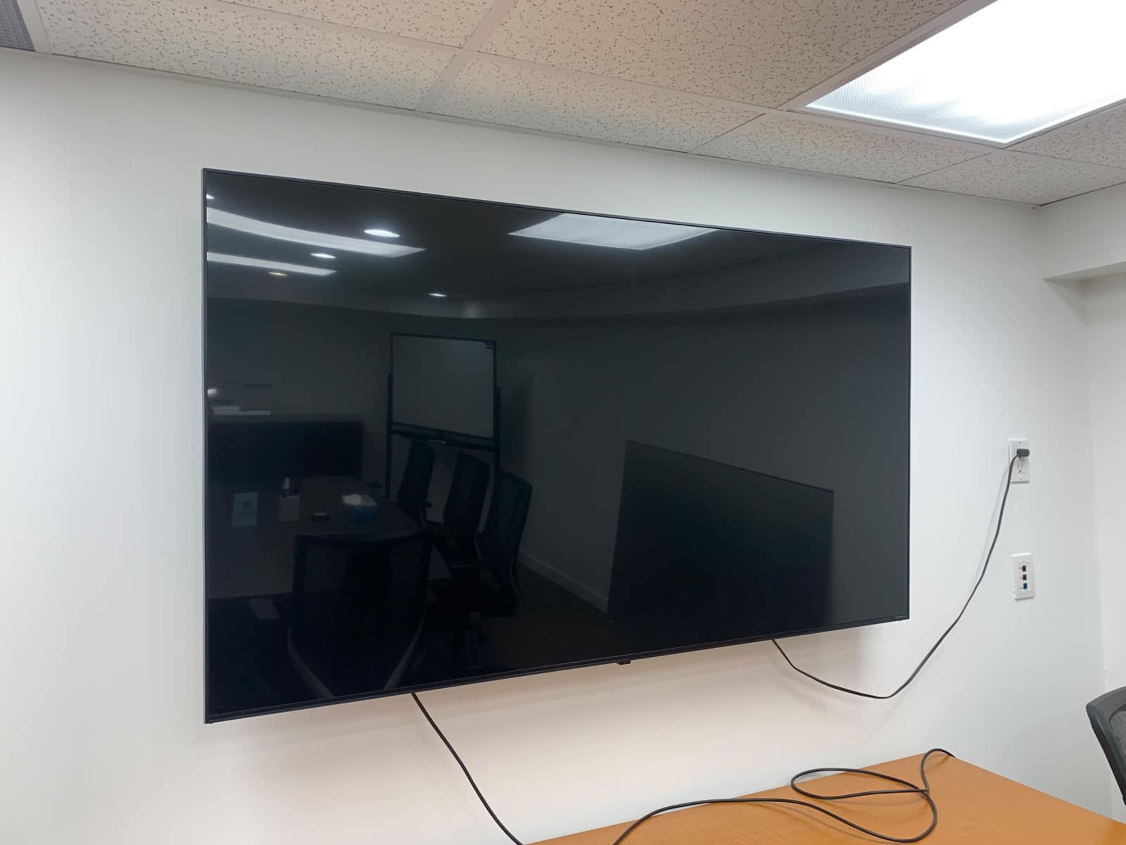 A large flat-screen television is mounted on a wall in an office conference room.
