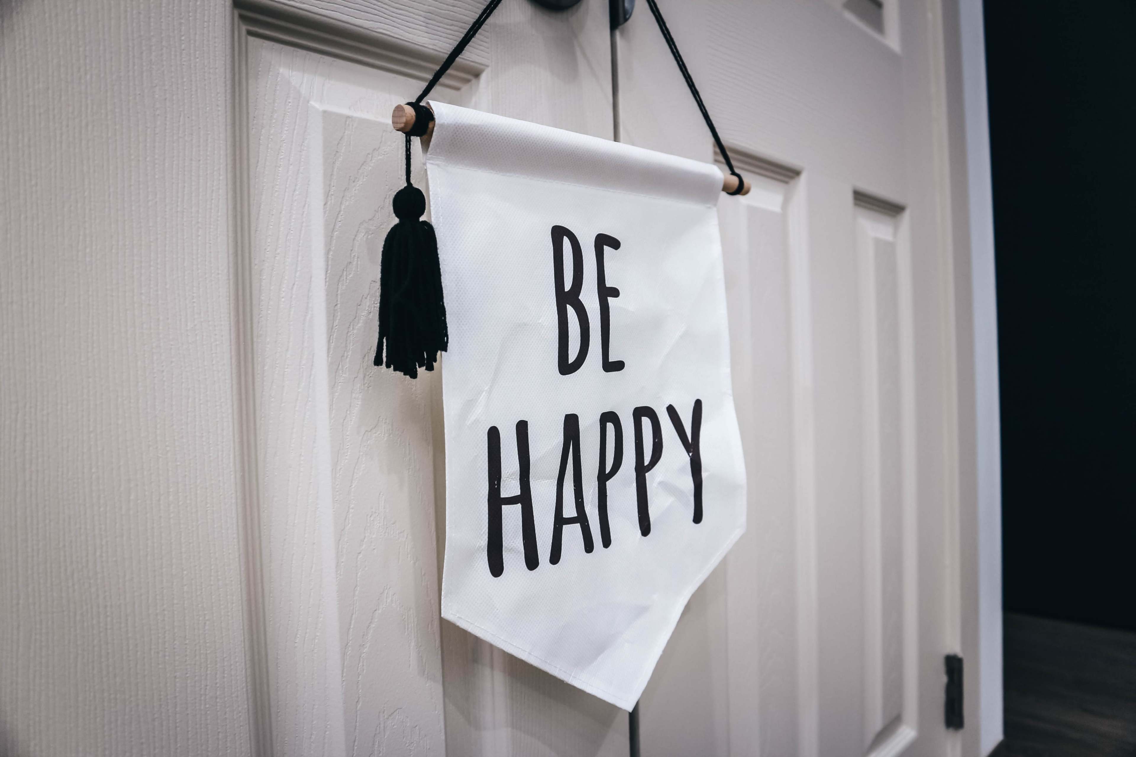 A white fabric banner with the words "BE HAPPY" is hanging from a door.