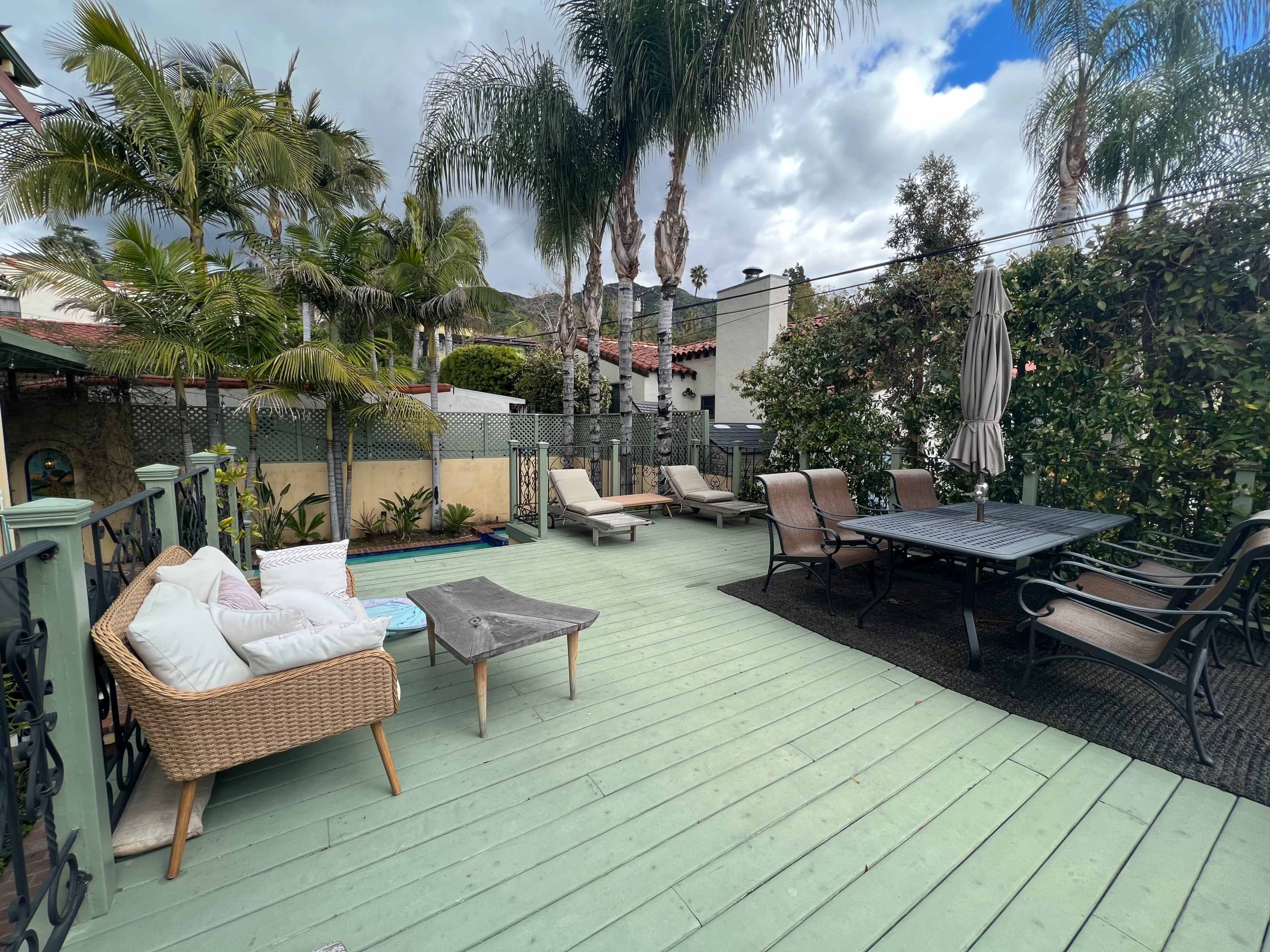 A patio area with outdoor seating, a dining table, palm trees, and lounge chairs near a small pool.