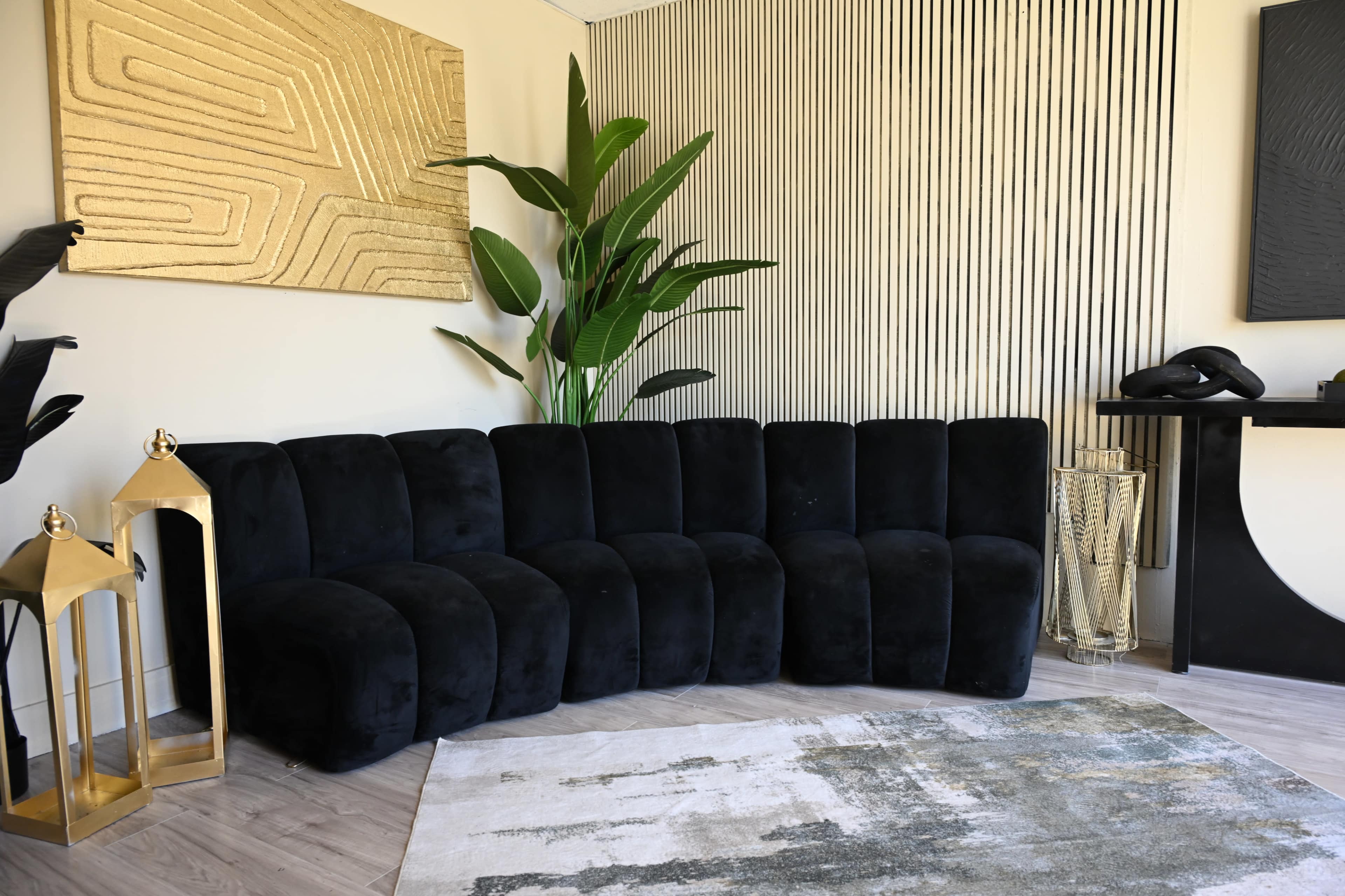 A black, sectional sofa is positioned in a modern living room with gold accents, a plant, and decorative lanterns.