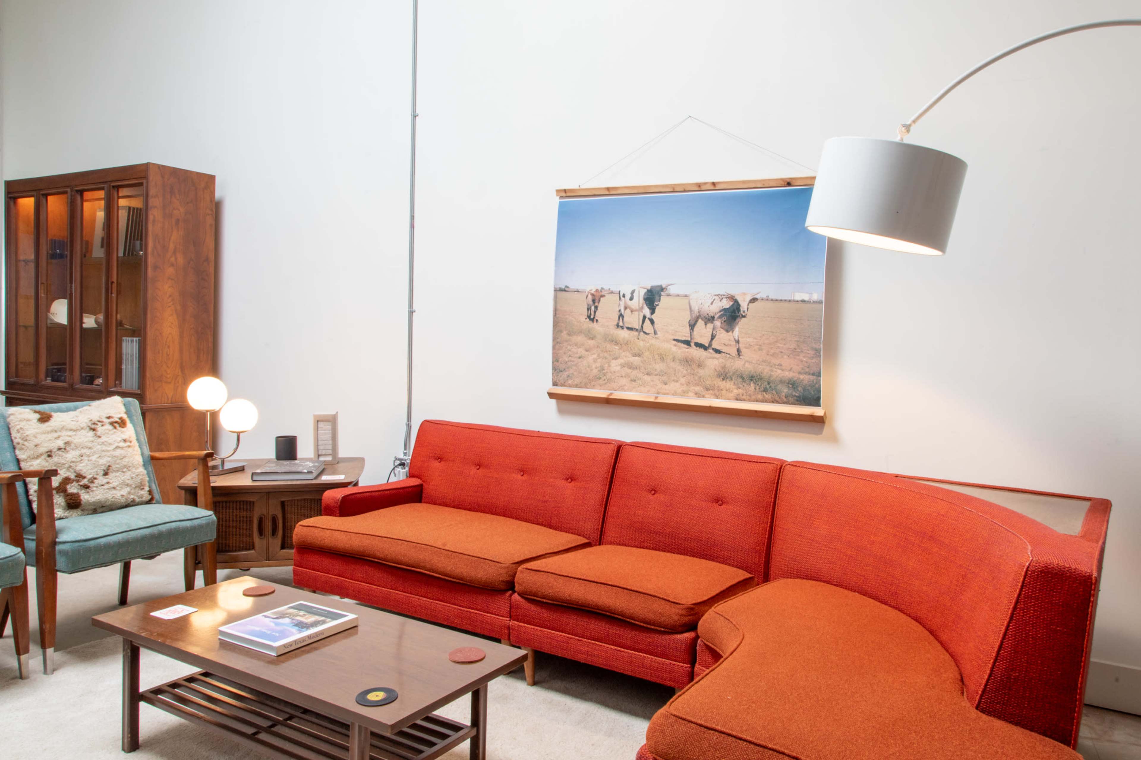 A mid-century modern living room featuring an orange sofa, a wooden coffee table, and a large photograph of cows on the wall.