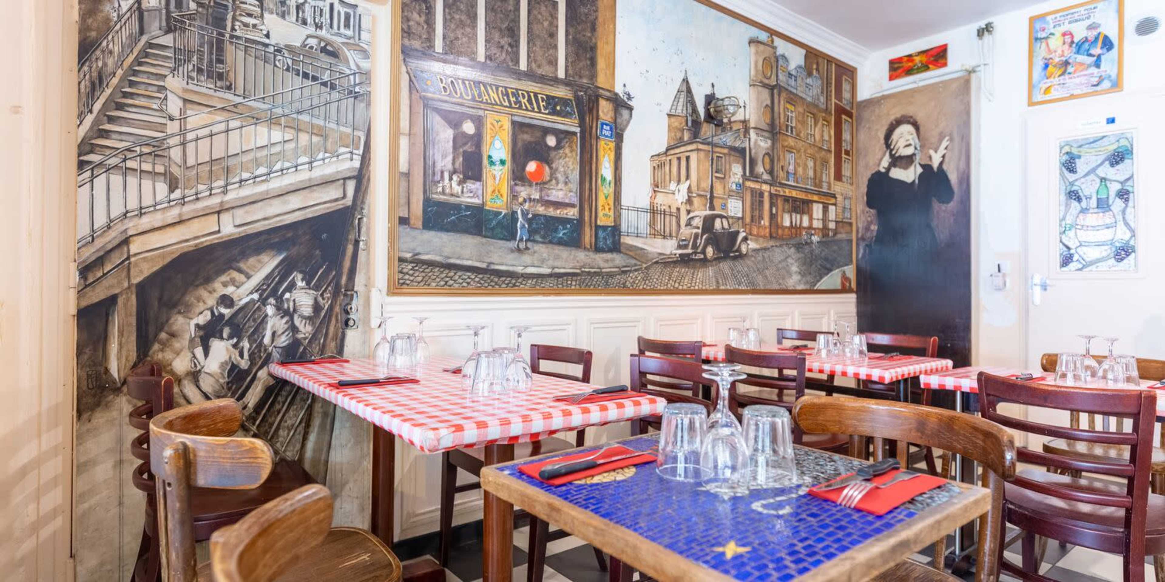 The image shows a restaurant interior with wooden tables covered in red-and-white checkered cloths and decorative murals on the walls.