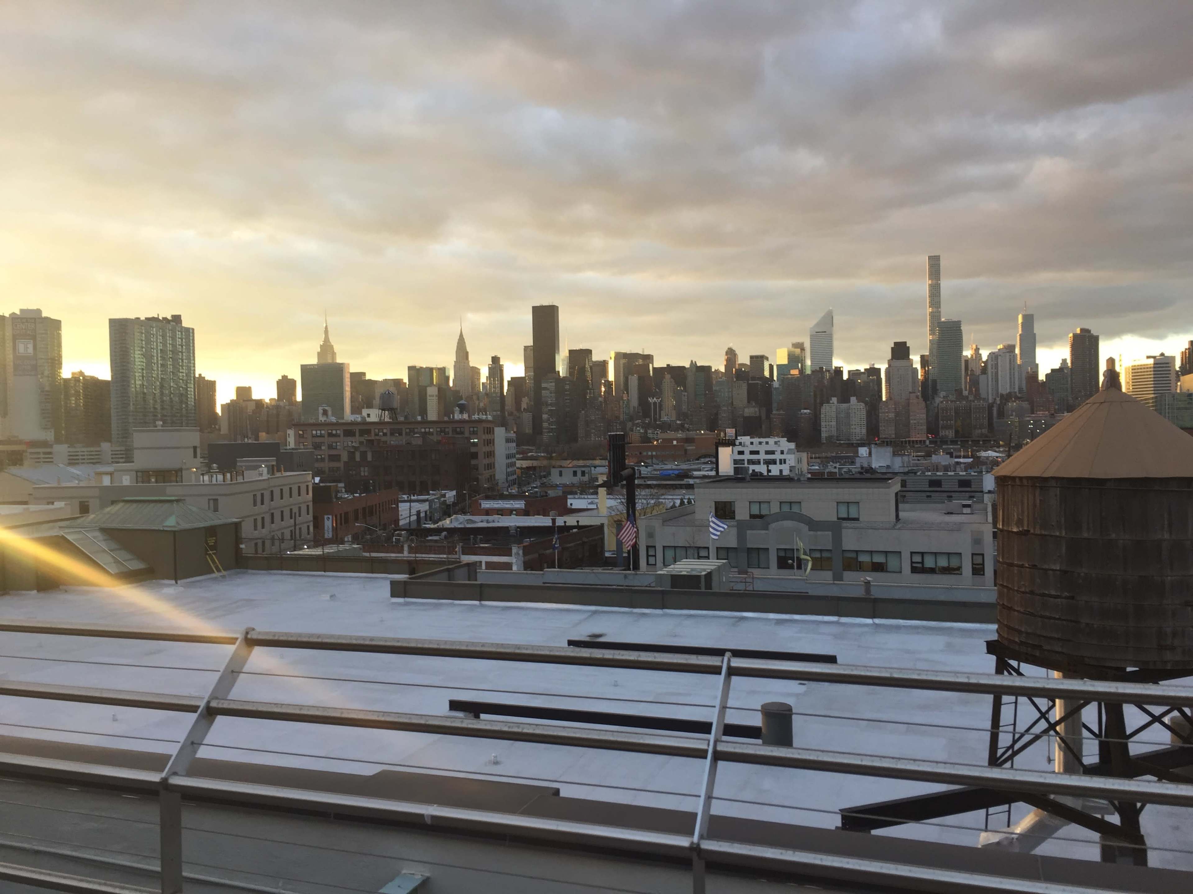 The image shows a view of the New York City skyline at sunset, with buildings and a water tower in the foreground.