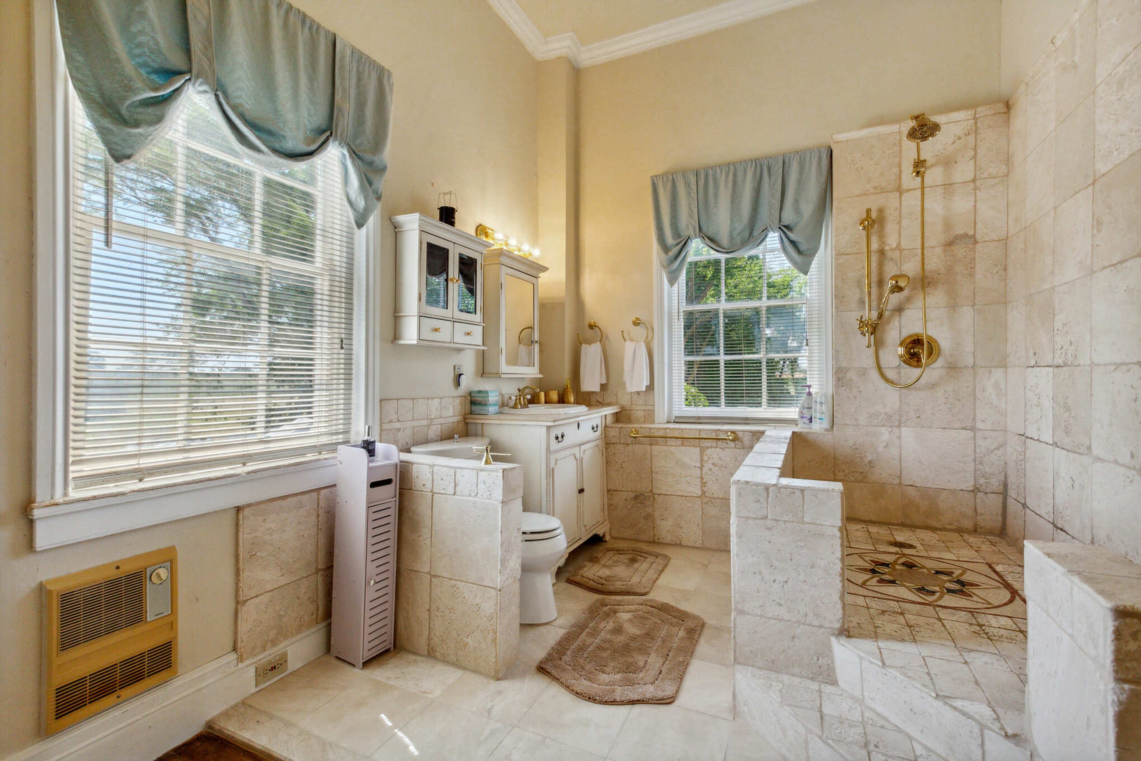 The bathroom features a shower area with a glass enclosure, a vanity with a mirror, and windows allowing natural light.