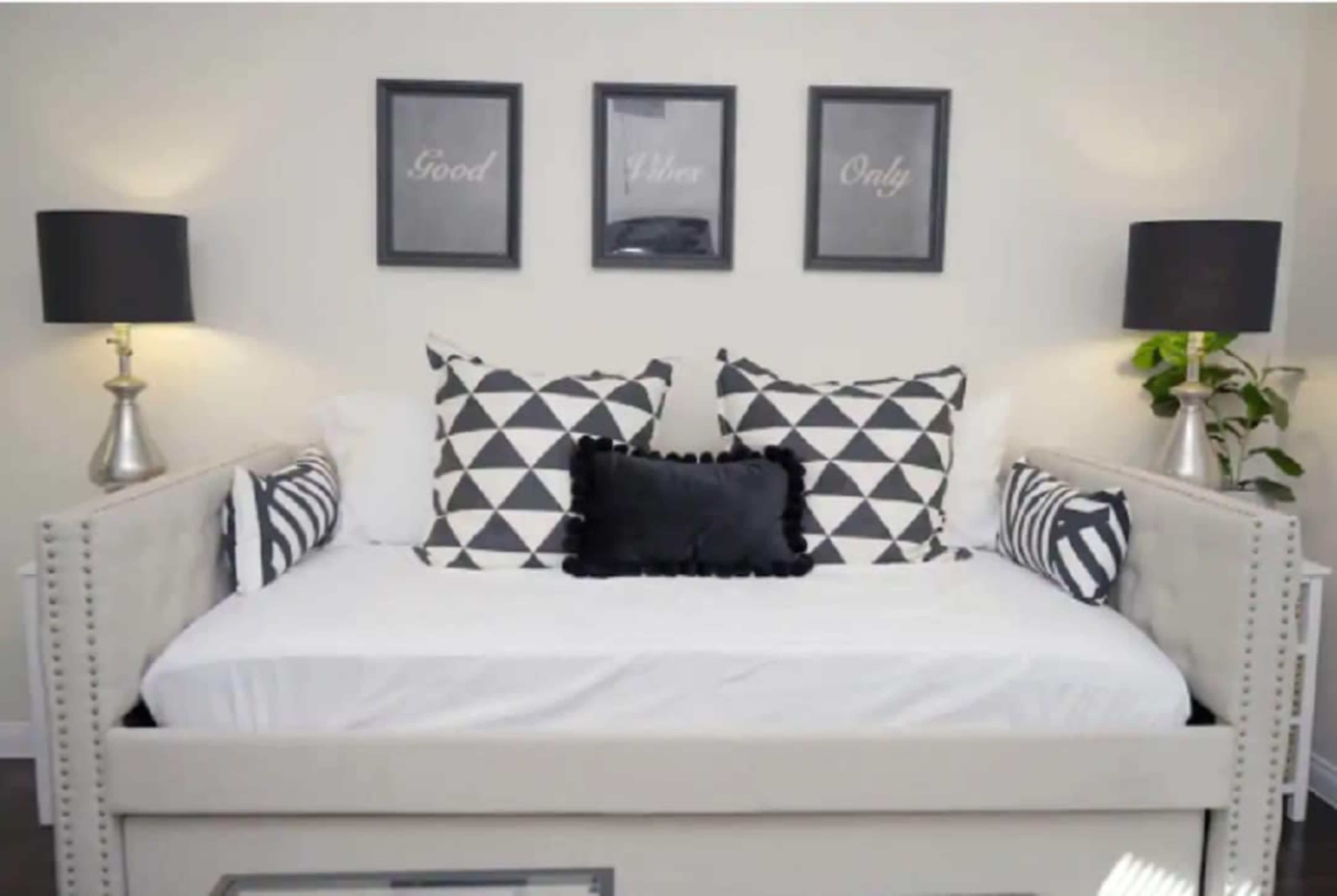 The image features a daybed adorned with patterned pillows, flanked by two lamps and three framed prints on the wall above.