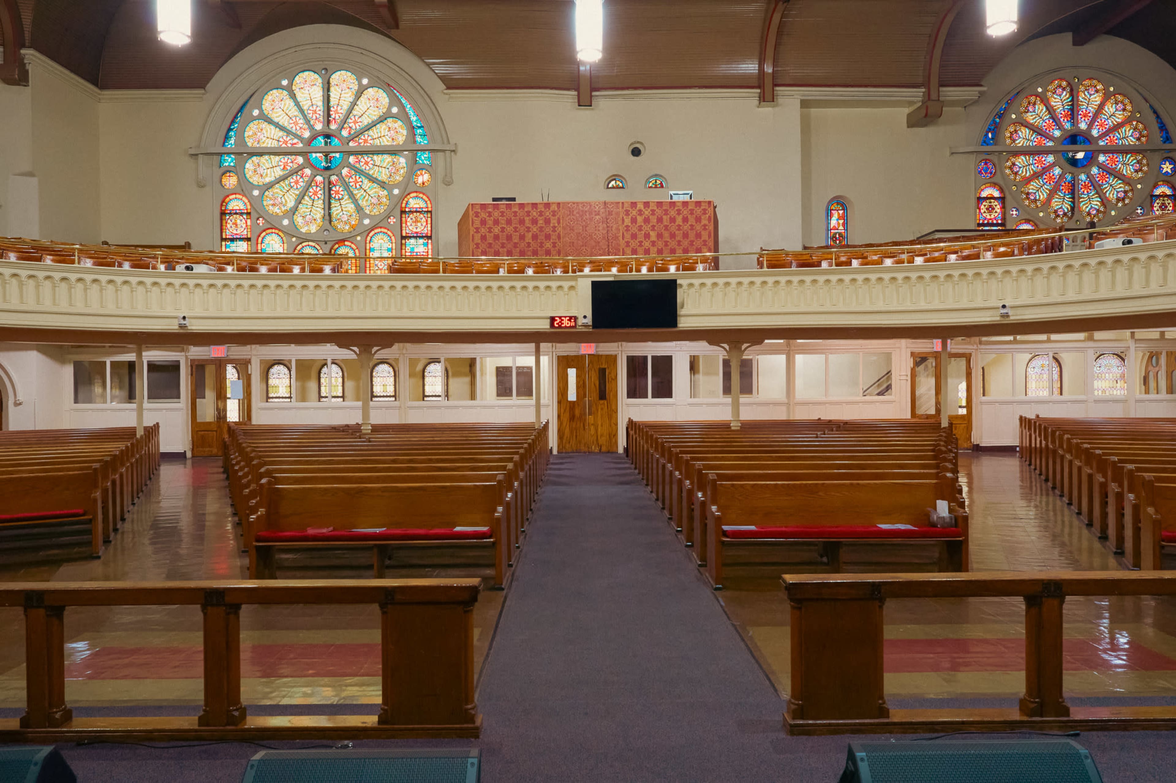 The image shows the interior of a church with wooden pews, a central aisle, and colorful stained glass windows illuminating the space.