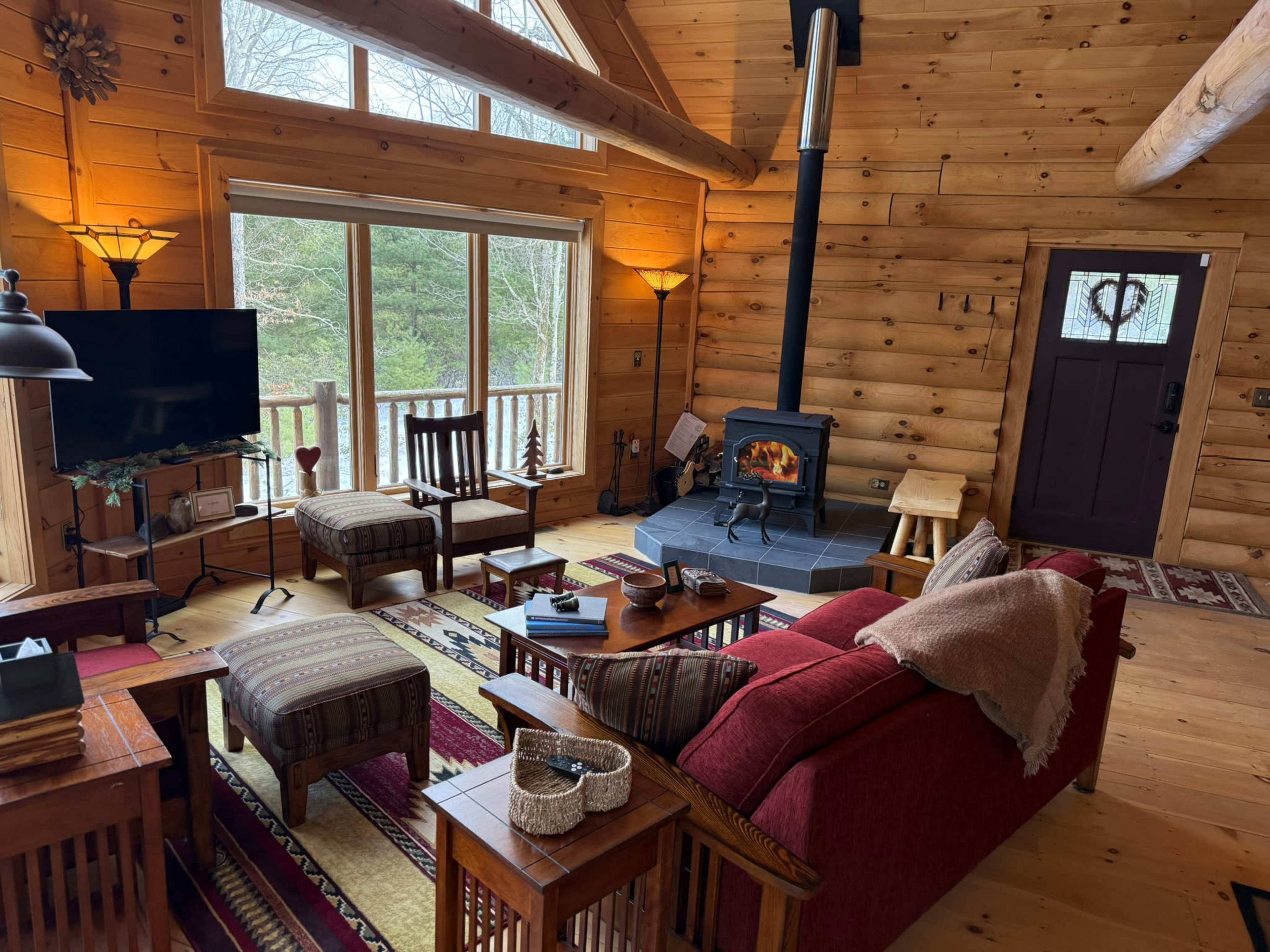 The image shows a cozy cabin interior with wooden walls, a stone fireplace, and comfortable seating surrounding a coffee table.