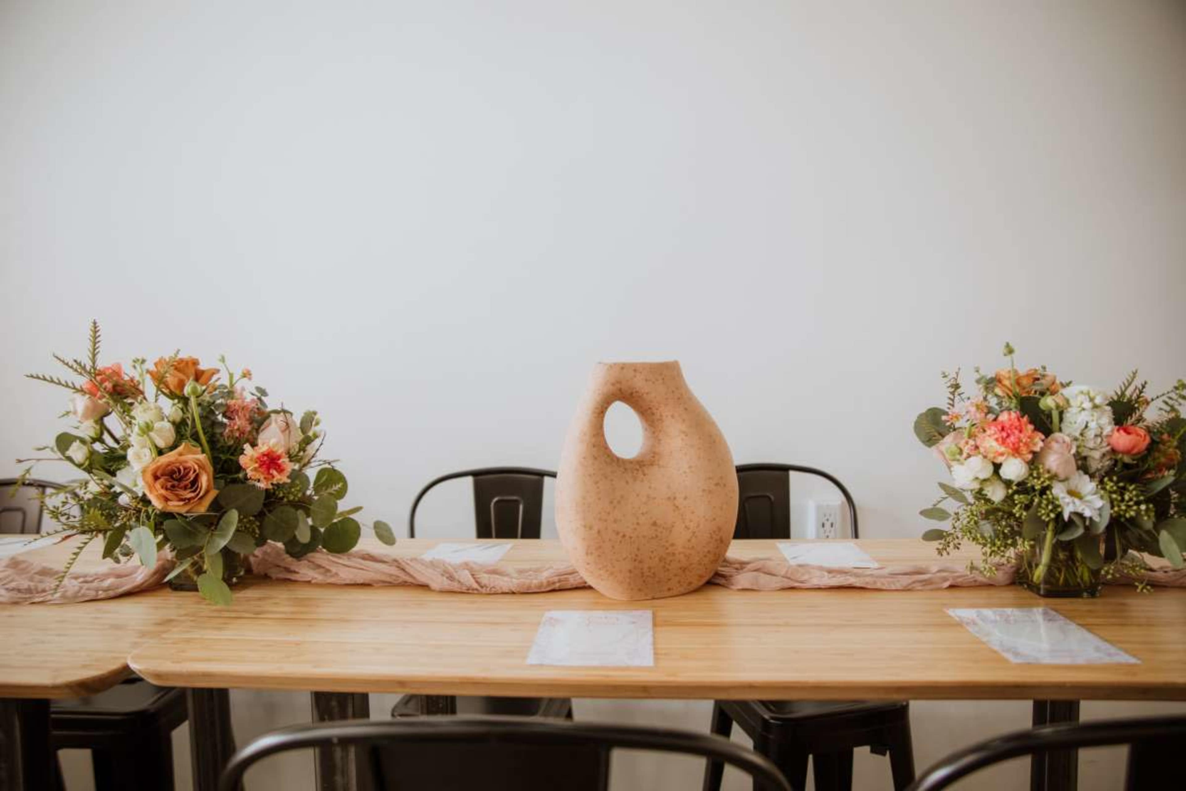 A wooden dining table is decorated with two floral arrangements and a central ceramic vase.