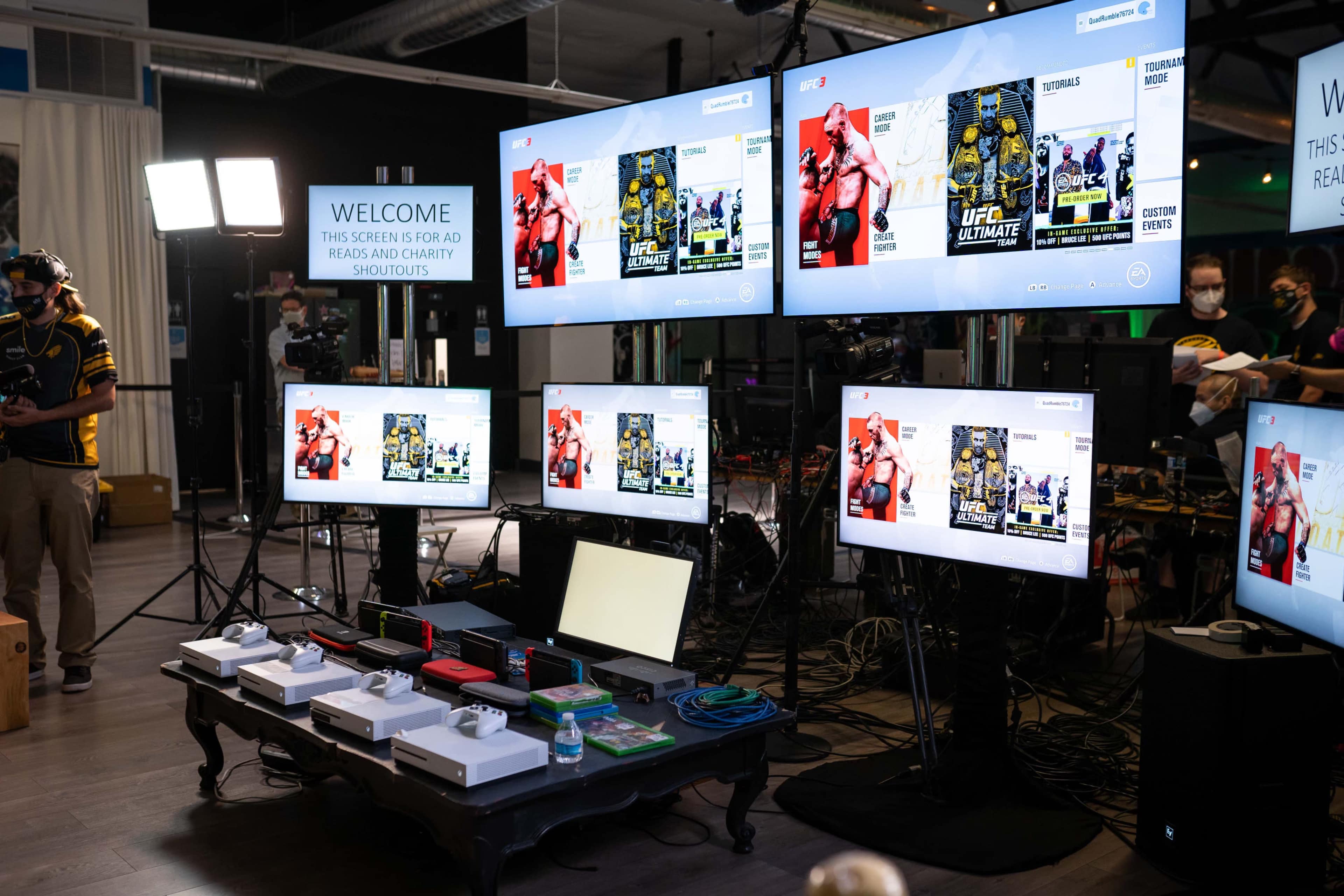 A display area featuring multiple televisions showcasing a video game, with a welcome sign and gaming equipment arranged on a table.