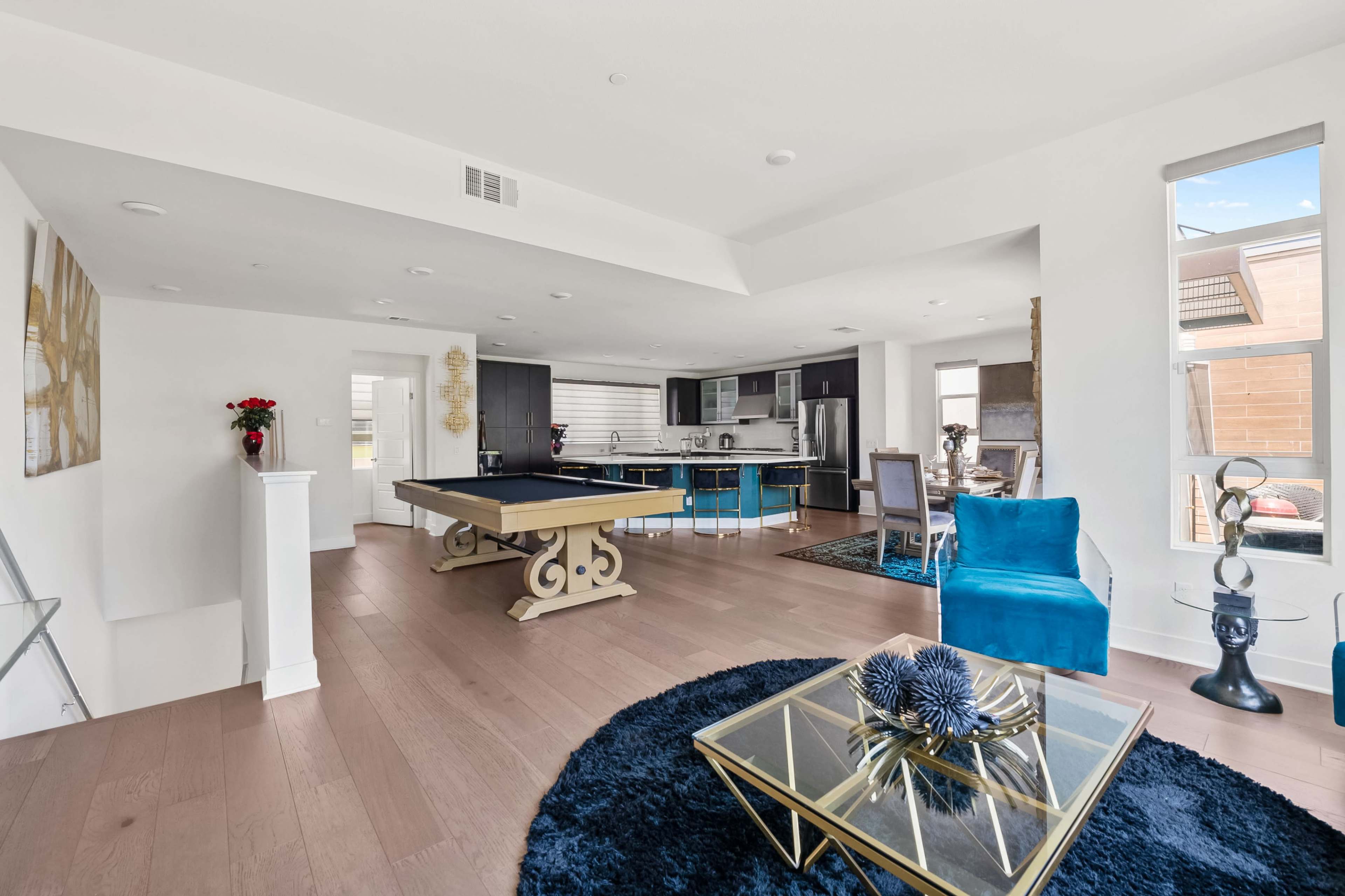 The image shows a modern open-concept living space featuring a billiards table, a dining area, a kitchen, and stylish furnishings.