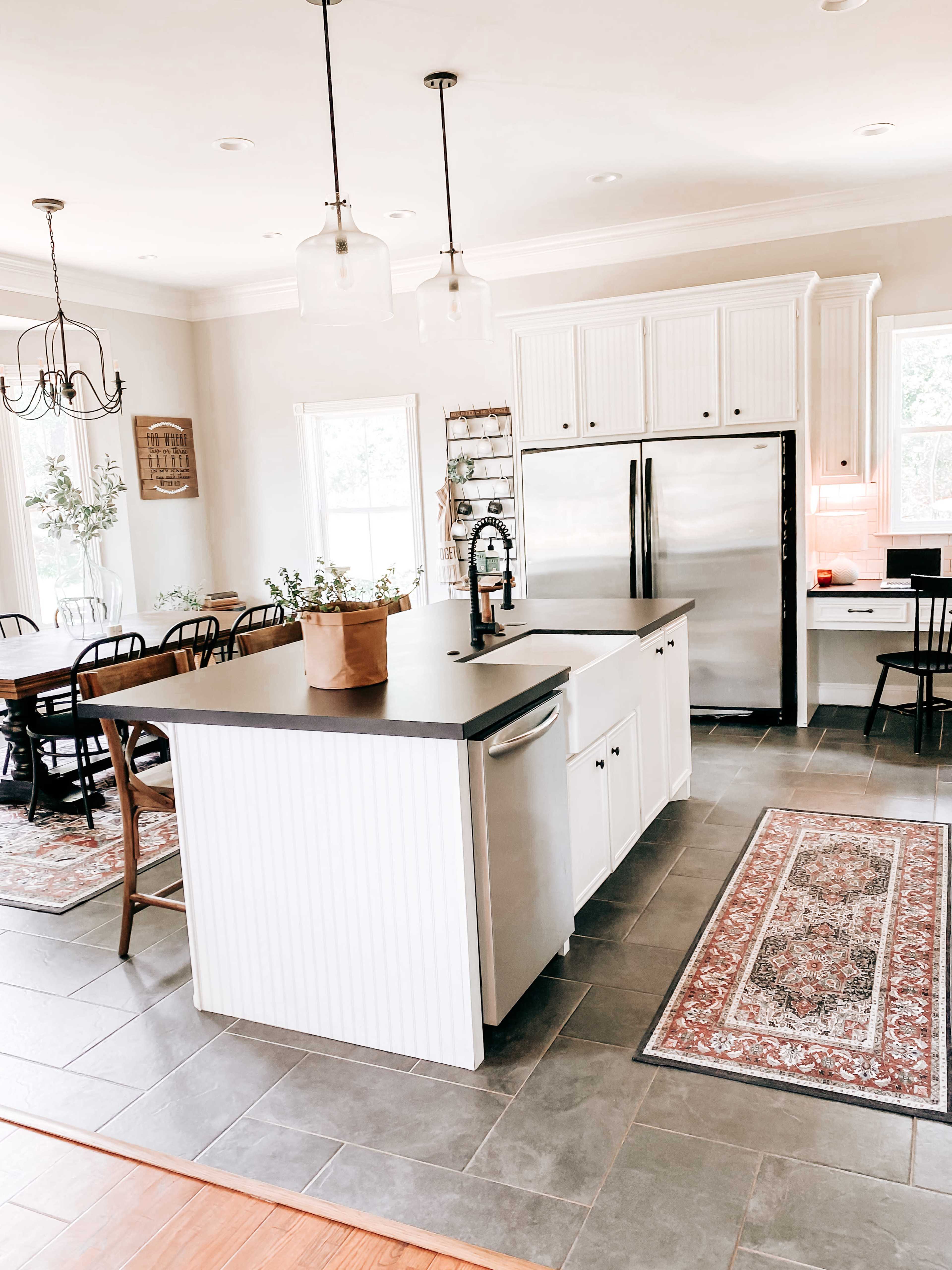 A modern kitchen features a central island with a dark countertop, white cabinetry, stainless steel appliances, and a combination of dining and prep areas.