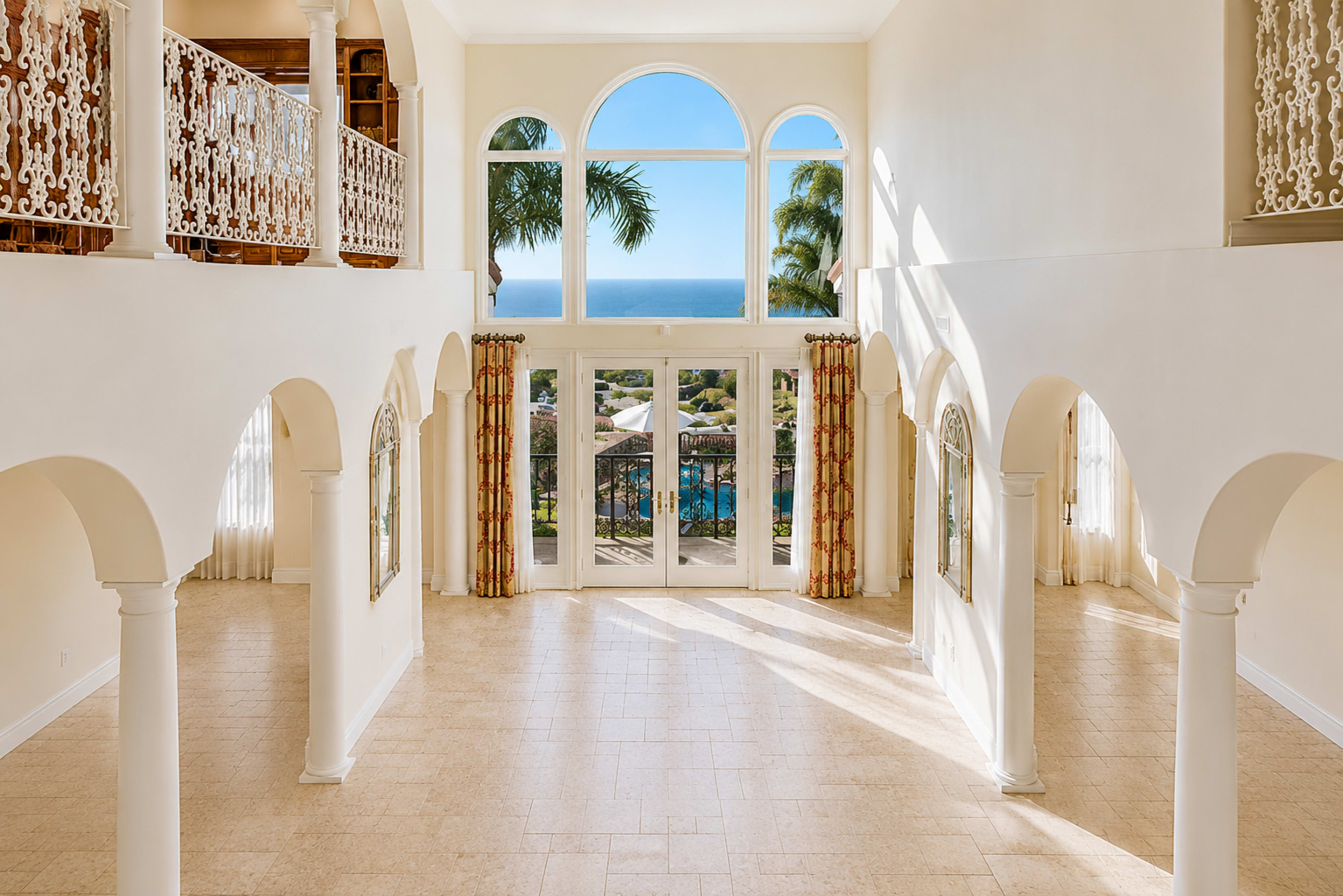 A spacious interior features large windows with ocean views, arches, and a high ceiling allowing natural light to illuminate the area.