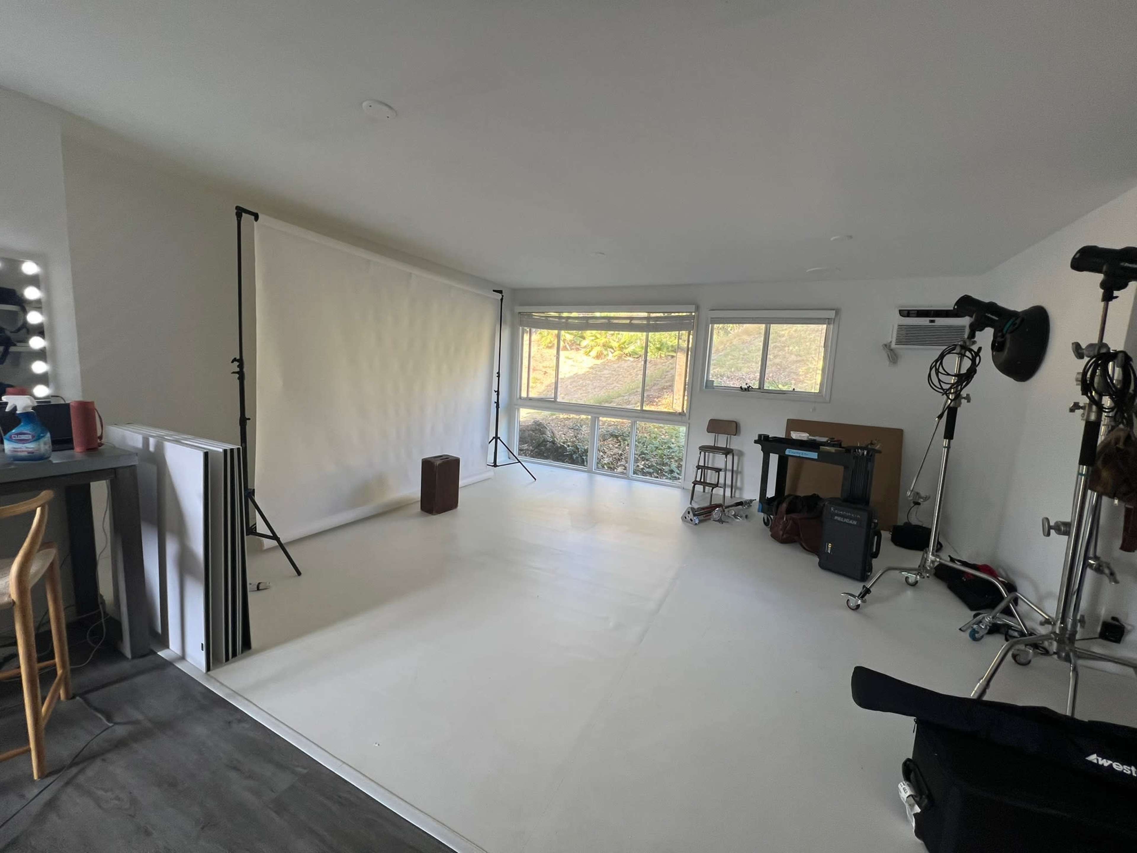 The image shows a bright, empty photography studio with a white backdrop, lighting equipment, and a few pieces of furniture.
