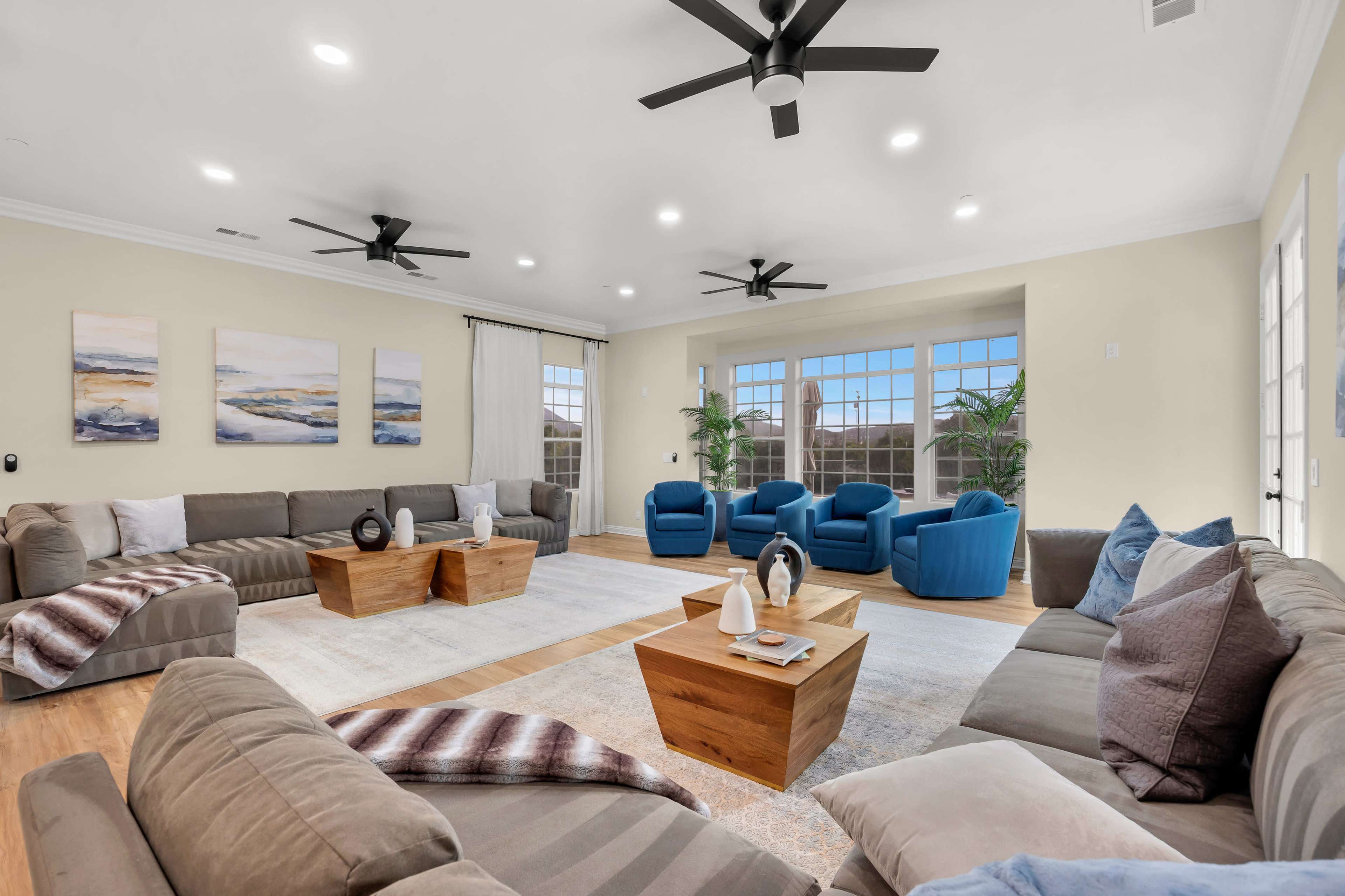 The living room features a spacious arrangement of dark sofas and blue chairs, with large windows bringing in natural light and wooden tables accentuating the design.