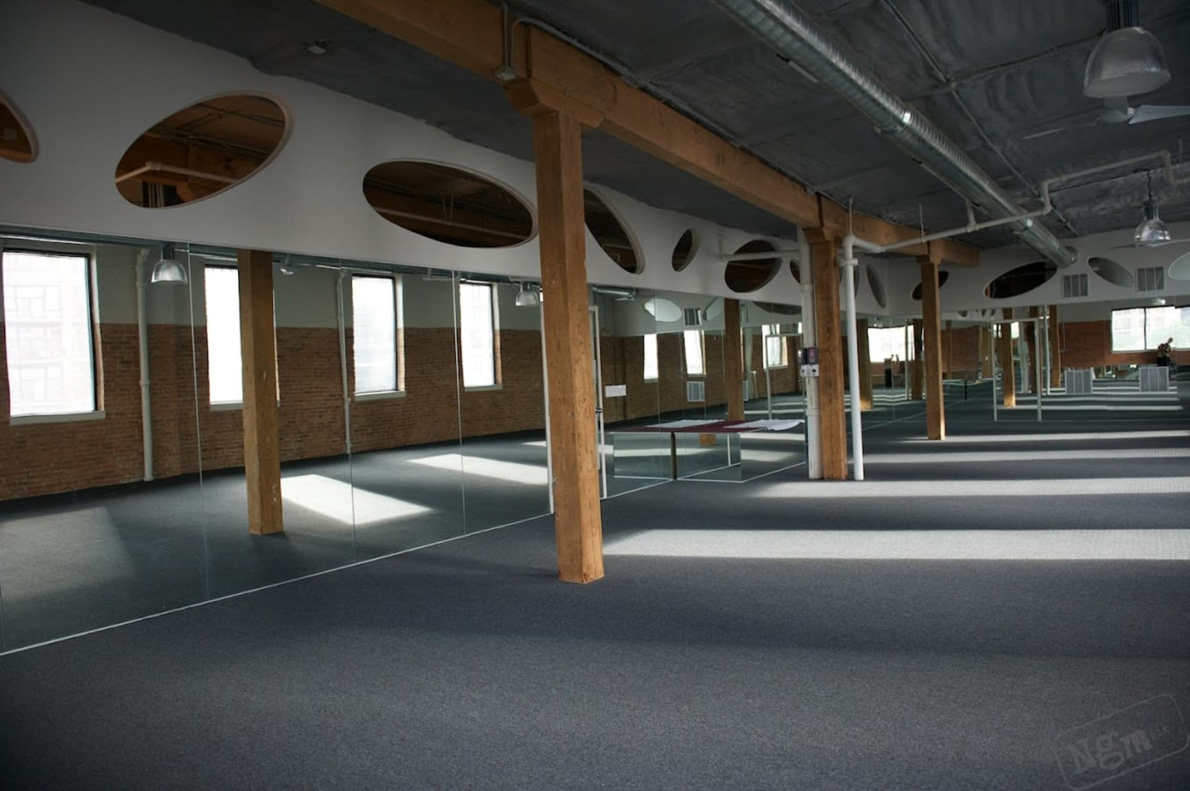 A spacious studio with wooden beams, large mirrors on one side, and windows allowing natural light to enter.