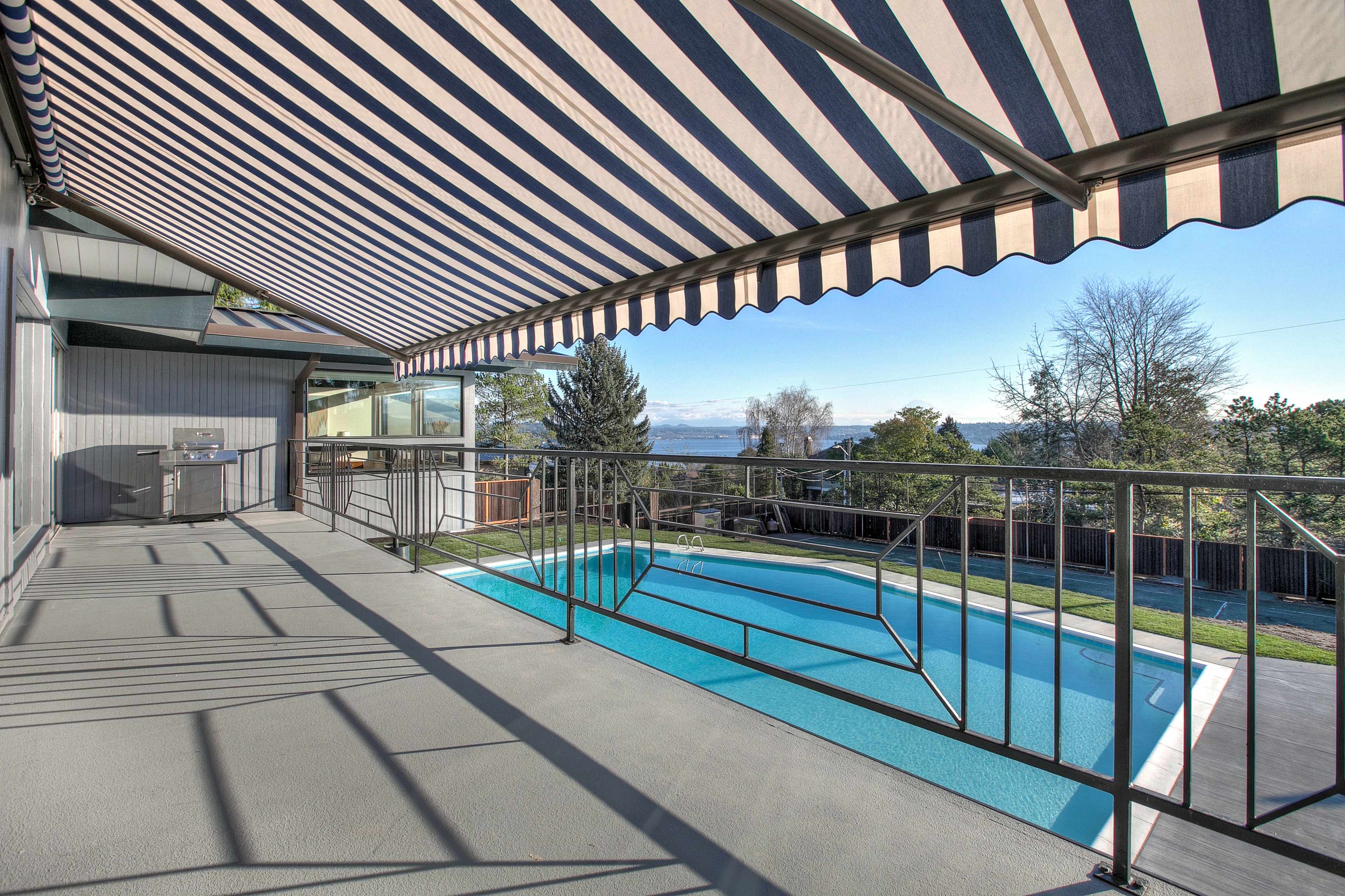 A patio with striped awnings overlooking a swimming pool and a landscaped yard.