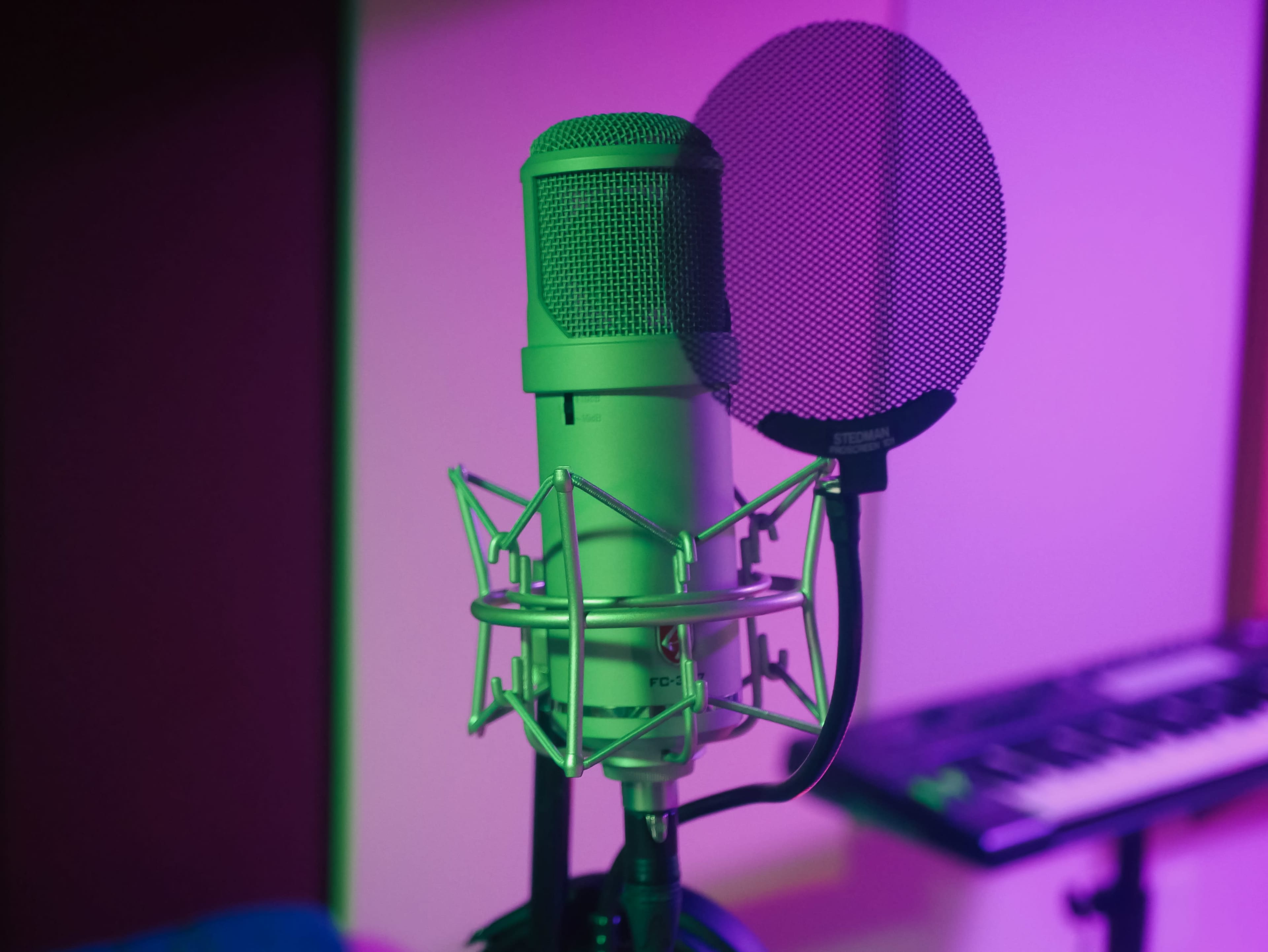 A microphone with a pop filter stands in a brightly lit recording studio.